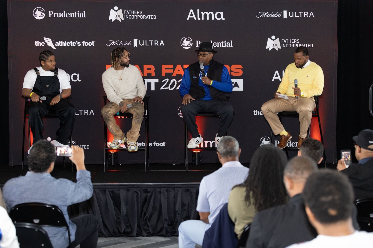 Panel discussion with speakers seated on stage at corporate event with sponsor logos displayed.