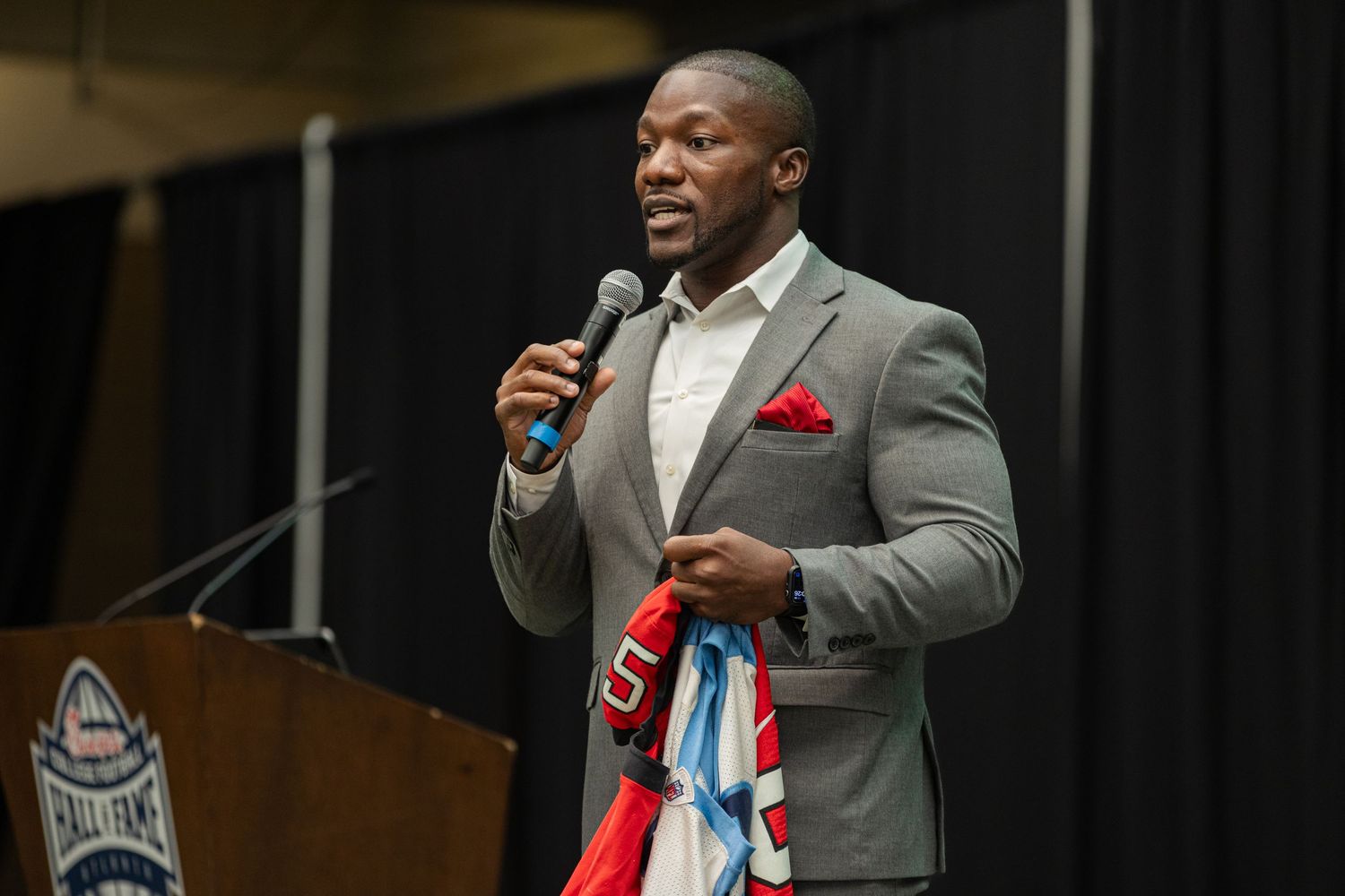Speaker in grey suit with red pocket square addresses audience at podium.