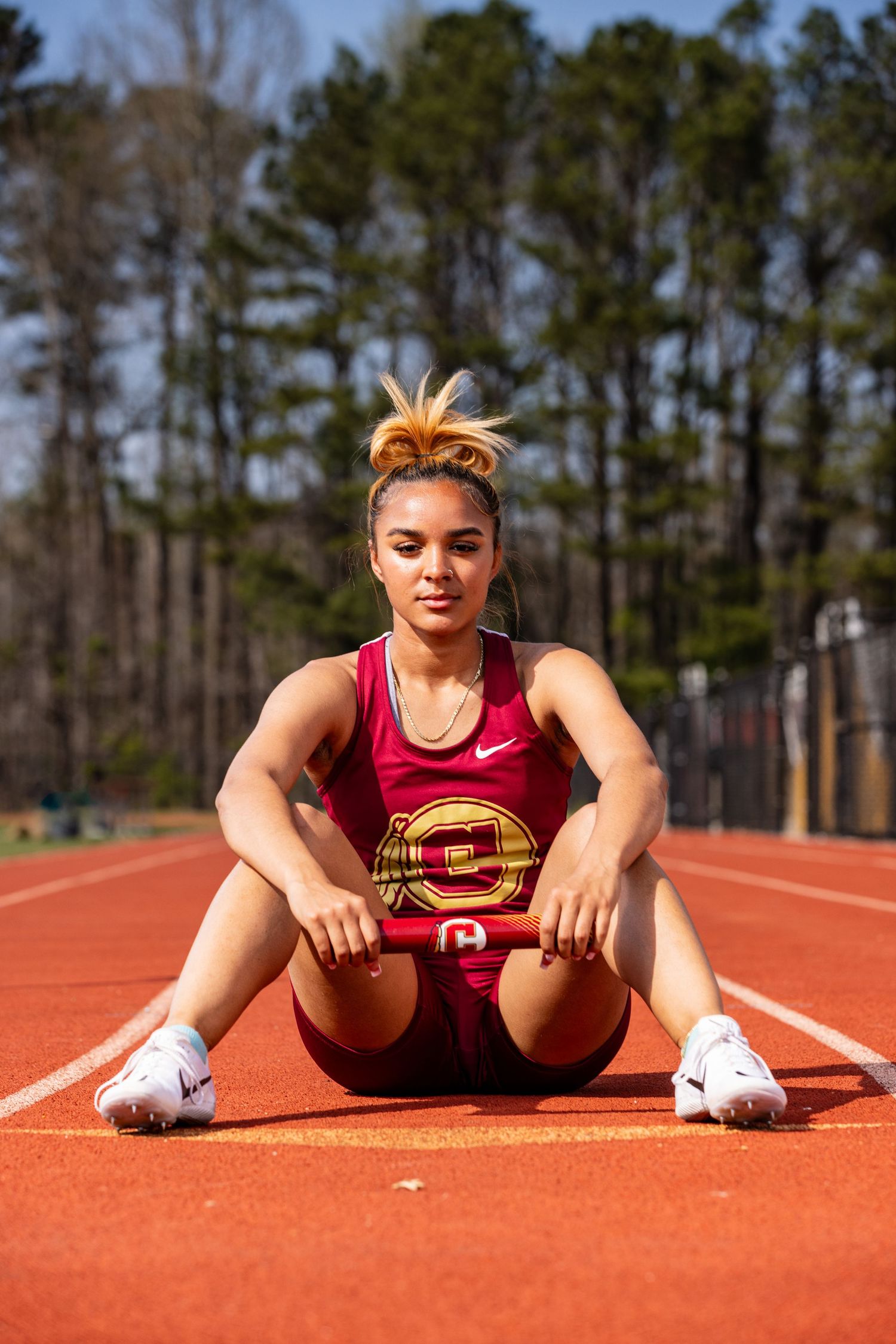 Athlete in red uniform sitting on track field during outdoor photoshoot.