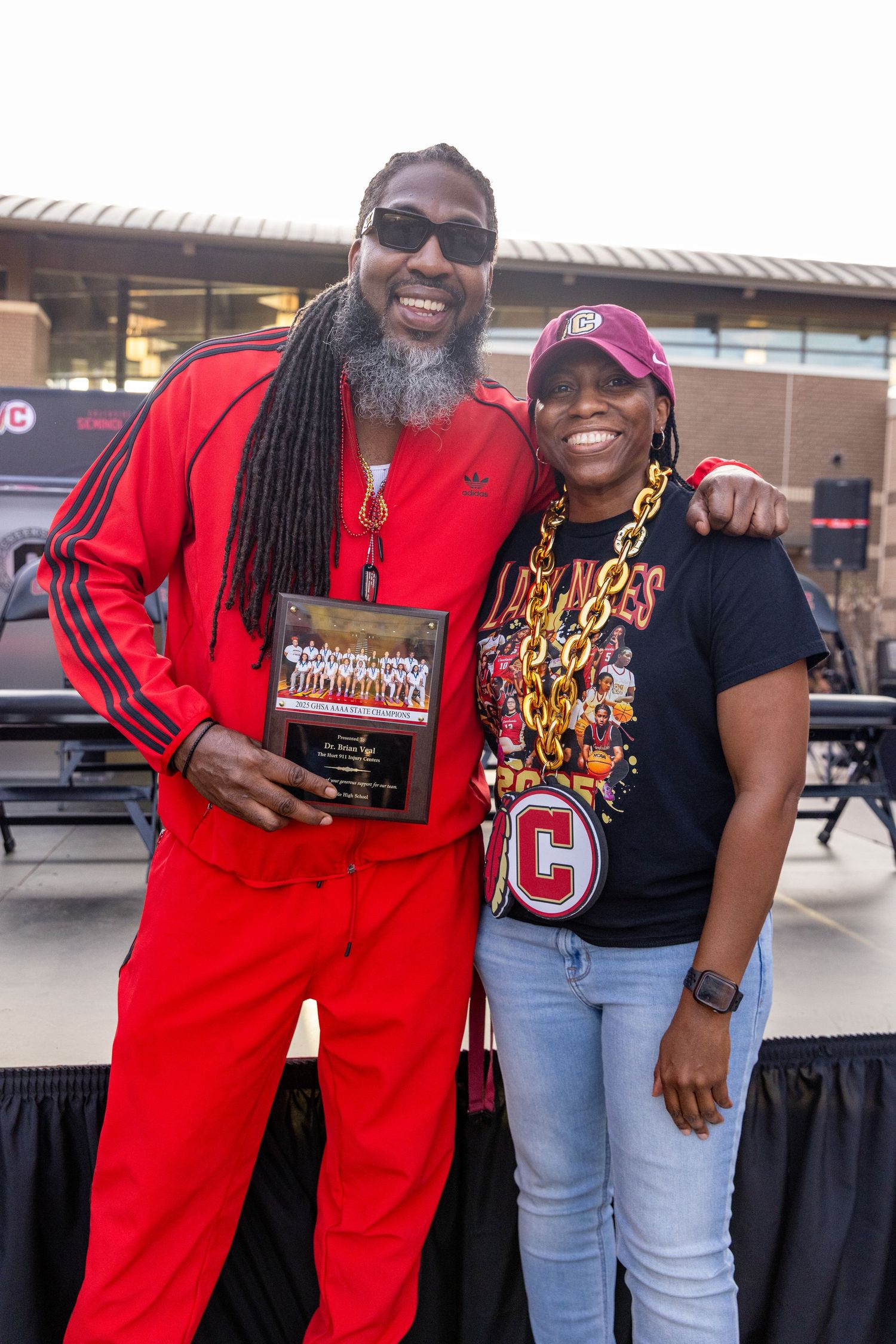 Two people posing with book at outdoor event wearing red and black outfits.