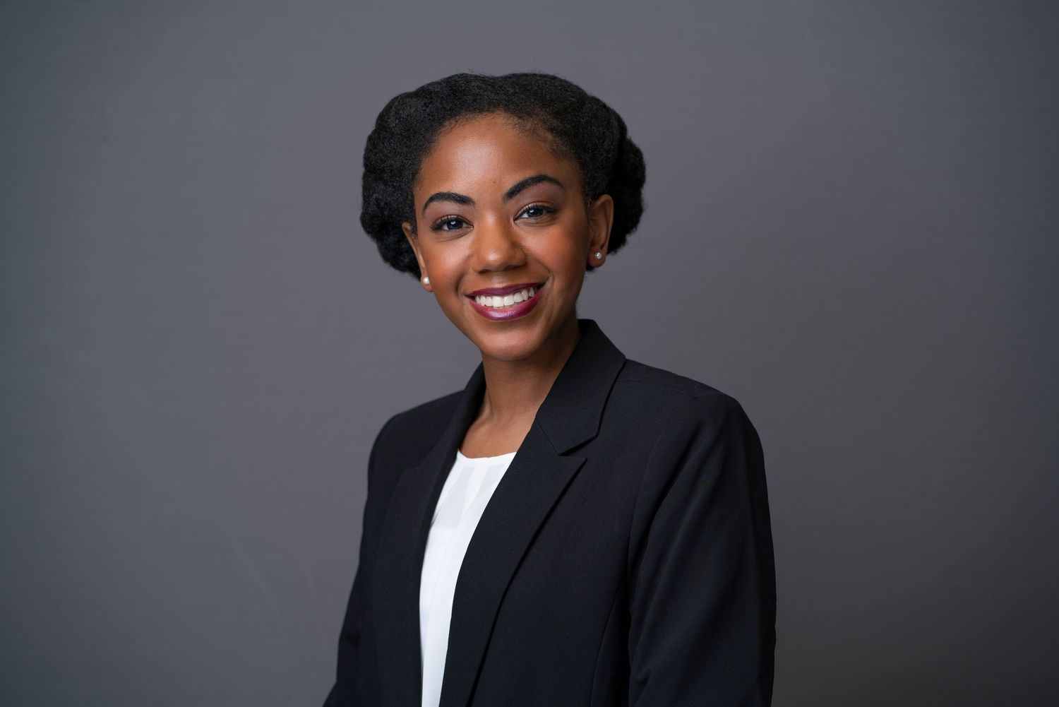 Professional portrait of businesswoman with braided hairstyle against gray backdrop.