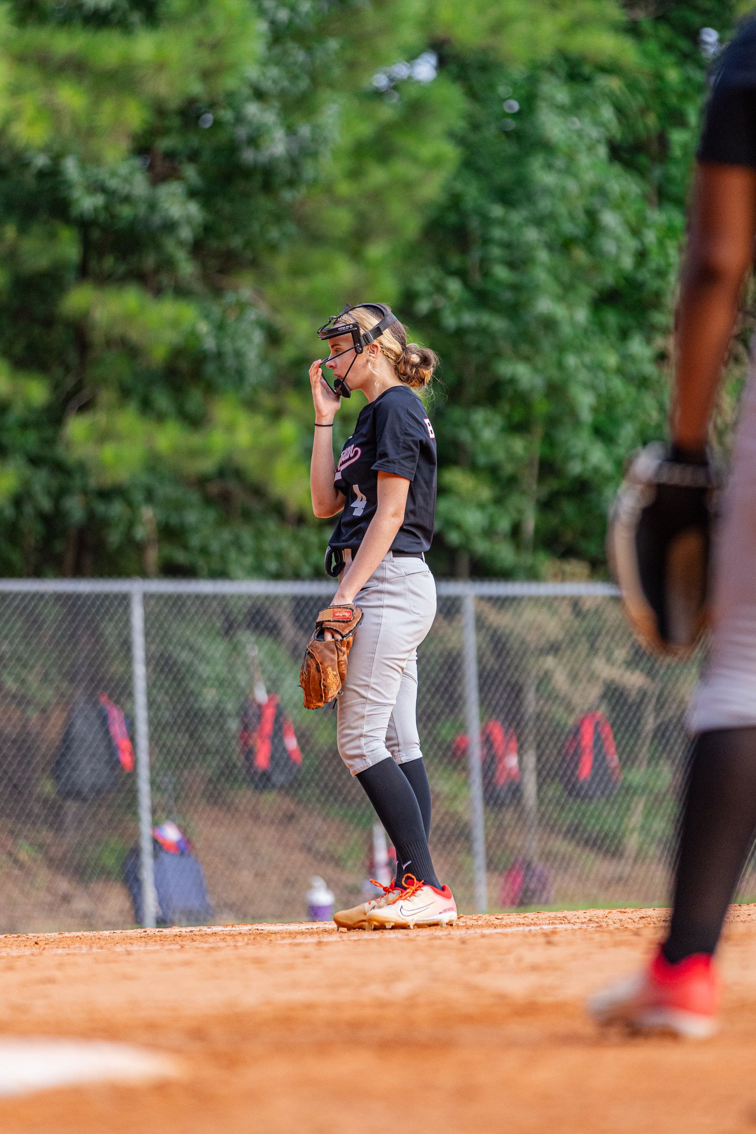 Softball pitcher in uniform stands on the mound during a game with a dirt infield.