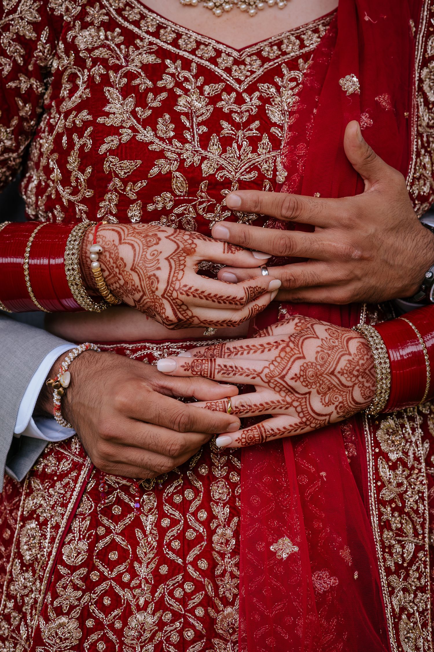 Intricate henna designs on hands with traditional red wedding attire and bangles.