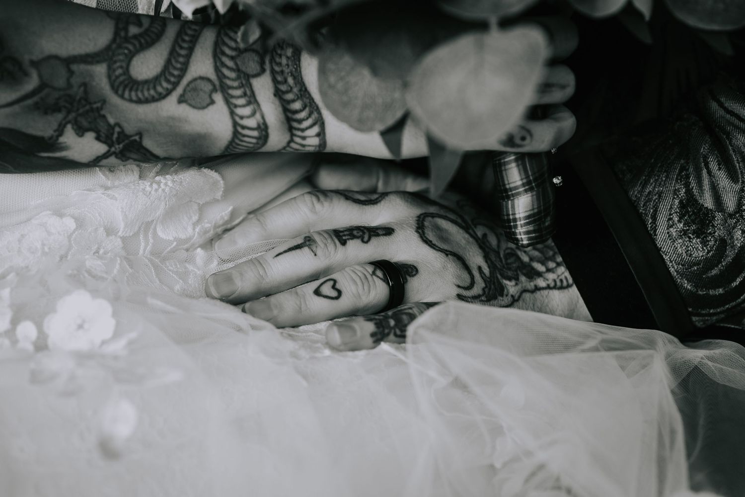 A close-up black and white photo of hands with wedding rings against lace fabric.