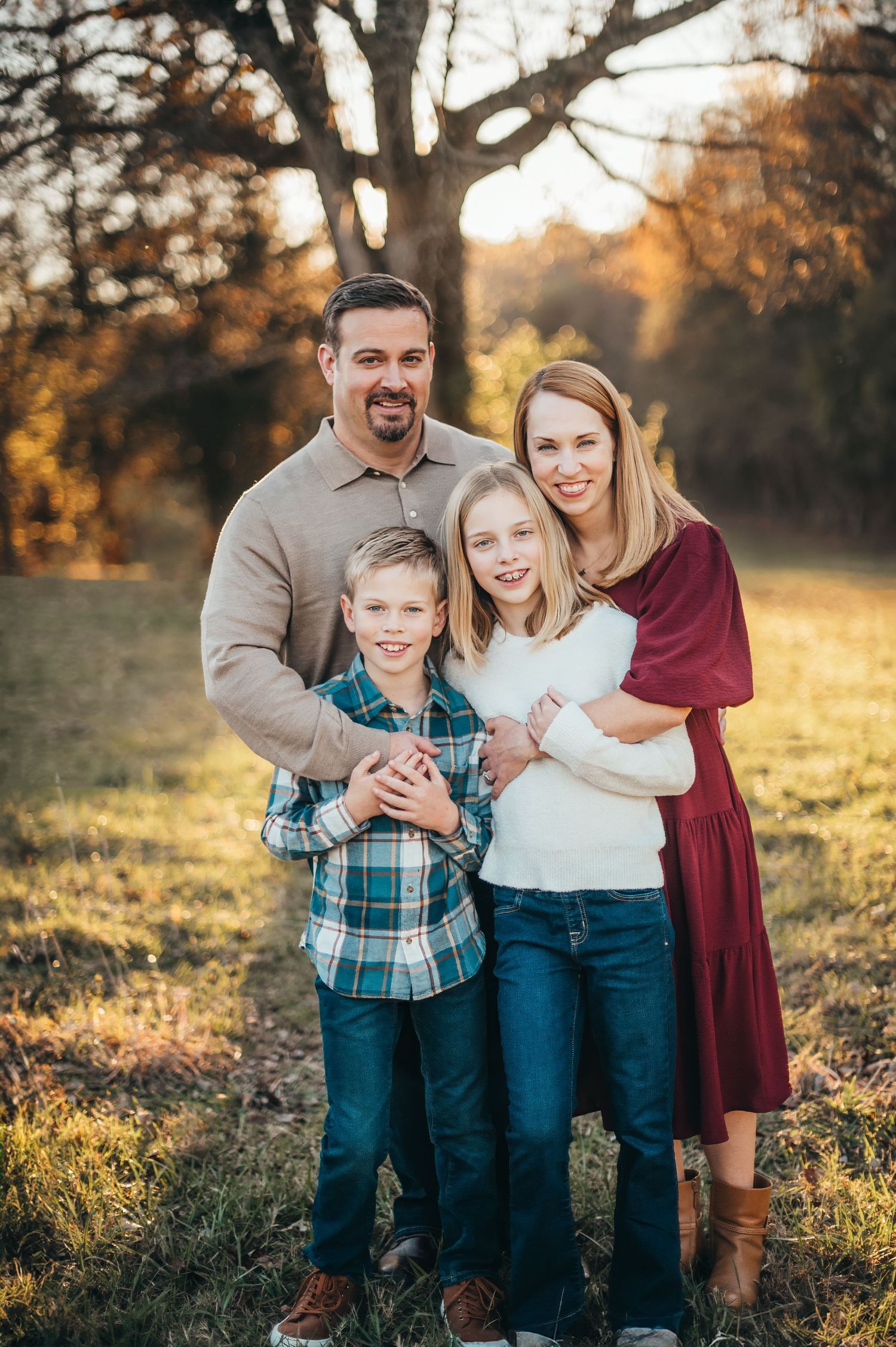 Family of four posing together outdoors during golden hour in autumn.