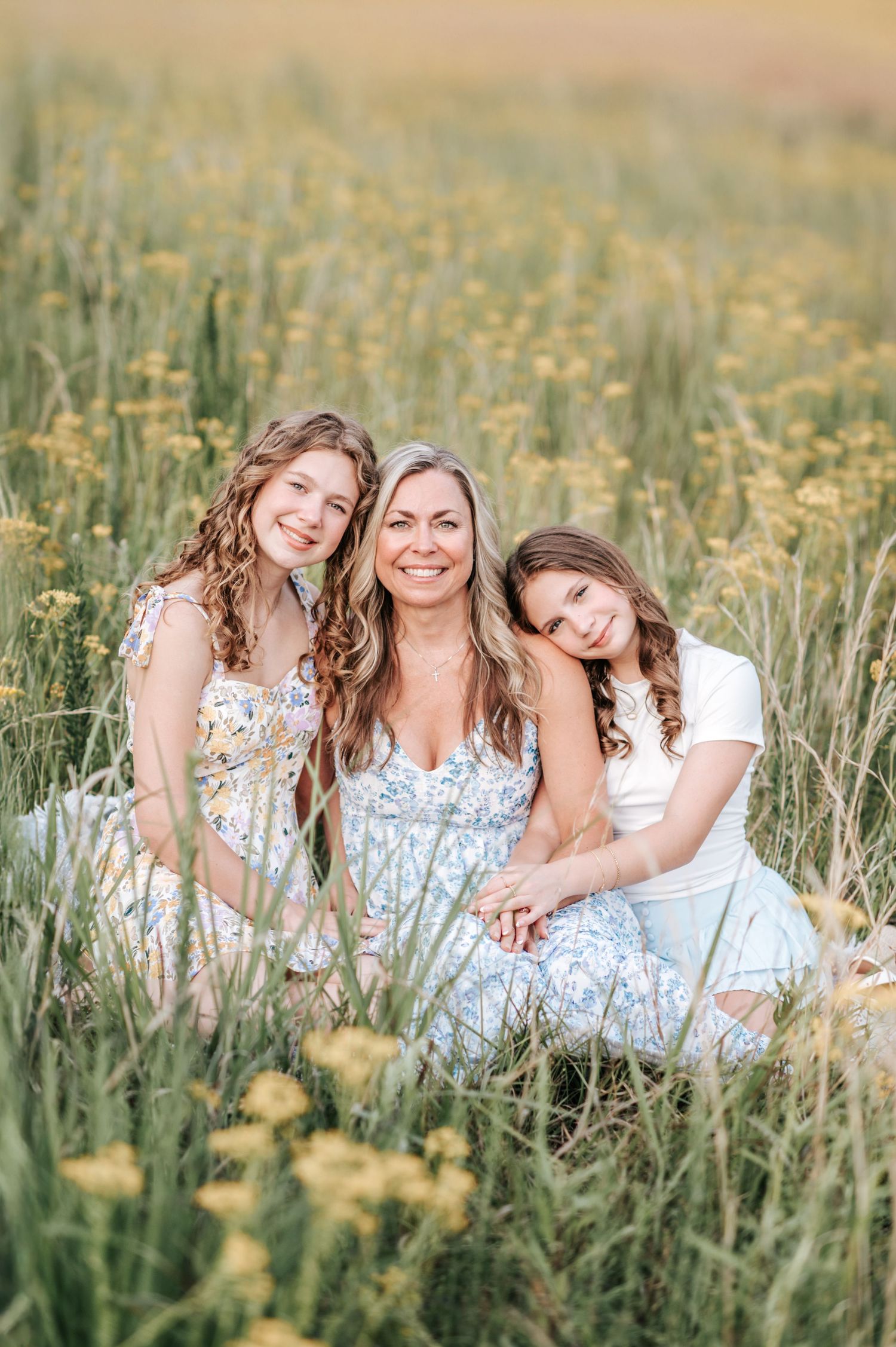 Family group sitting together in flowing dresses among wildflowers at sunset.