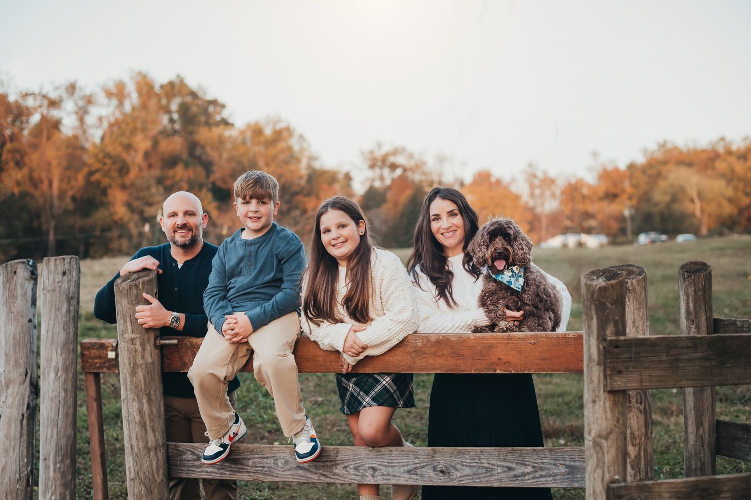 Group sitting on wooden fence at sunset with their dog.