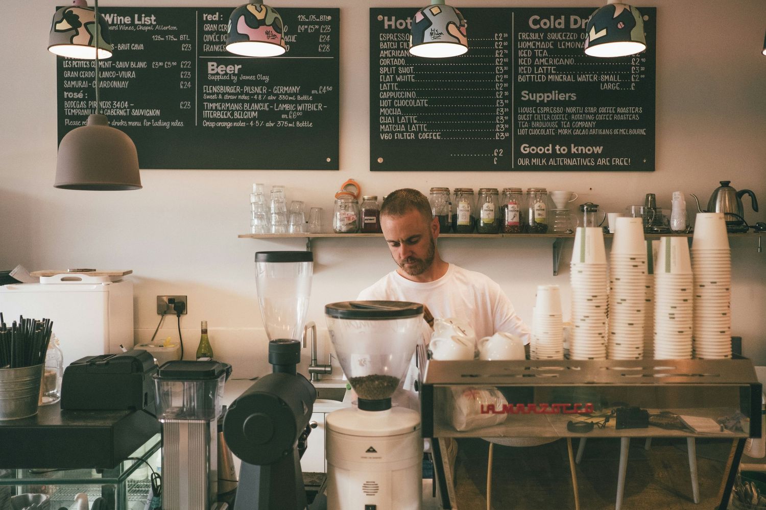 A cozy coffee shop interior with chalkboard menus, coffee equipment, and stacked cups along a wooden counter.