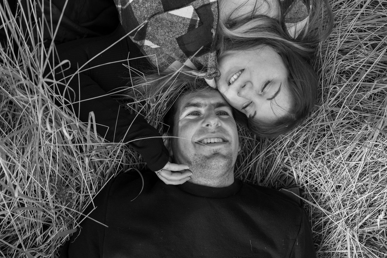A black and white photo of people lying down in tall grass, smiling while looking down at the camera.