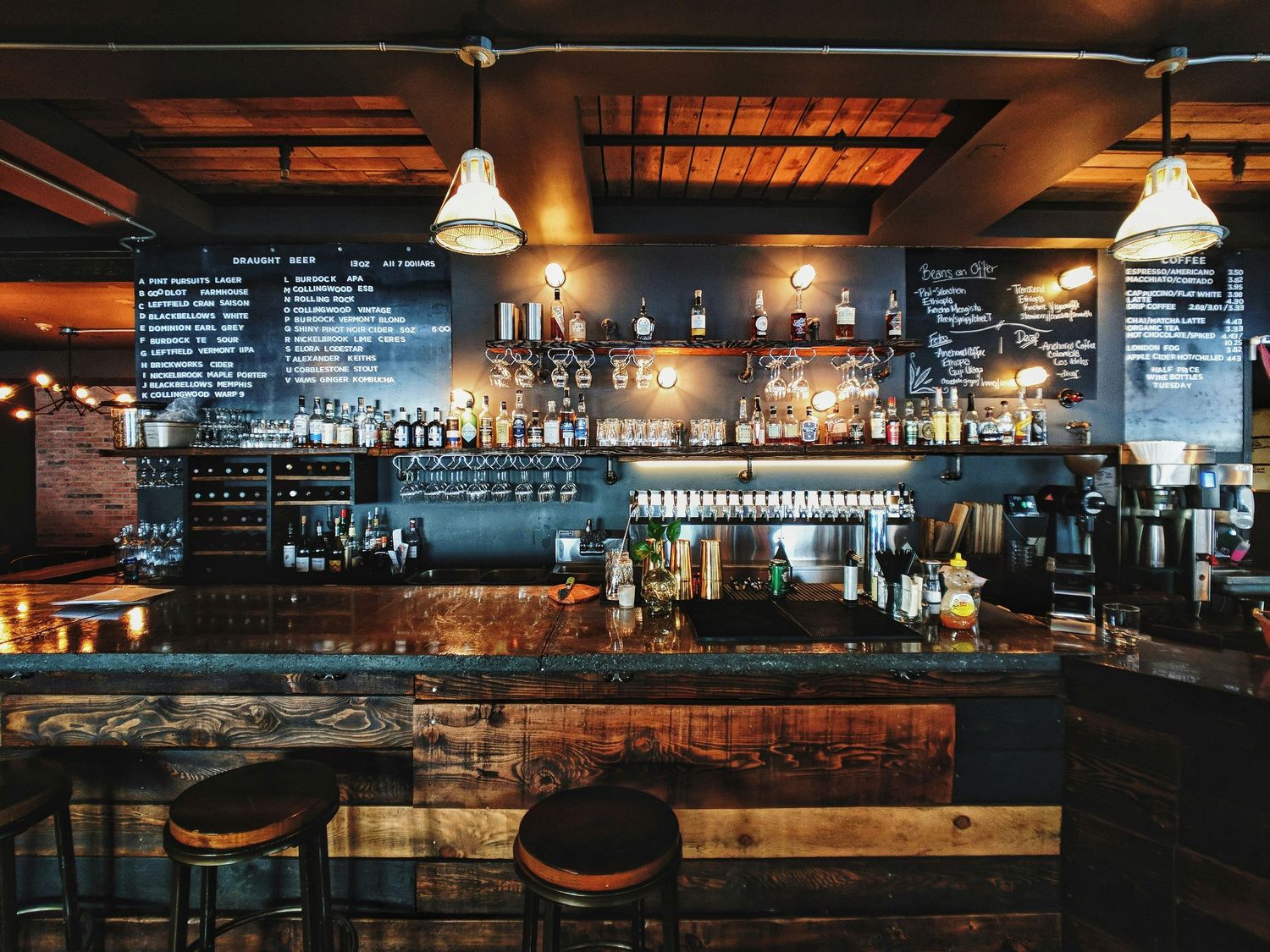 Cozy bar interior with chalkboard menus, wooden counter, and industrial pendant lighting creating warm ambiance.