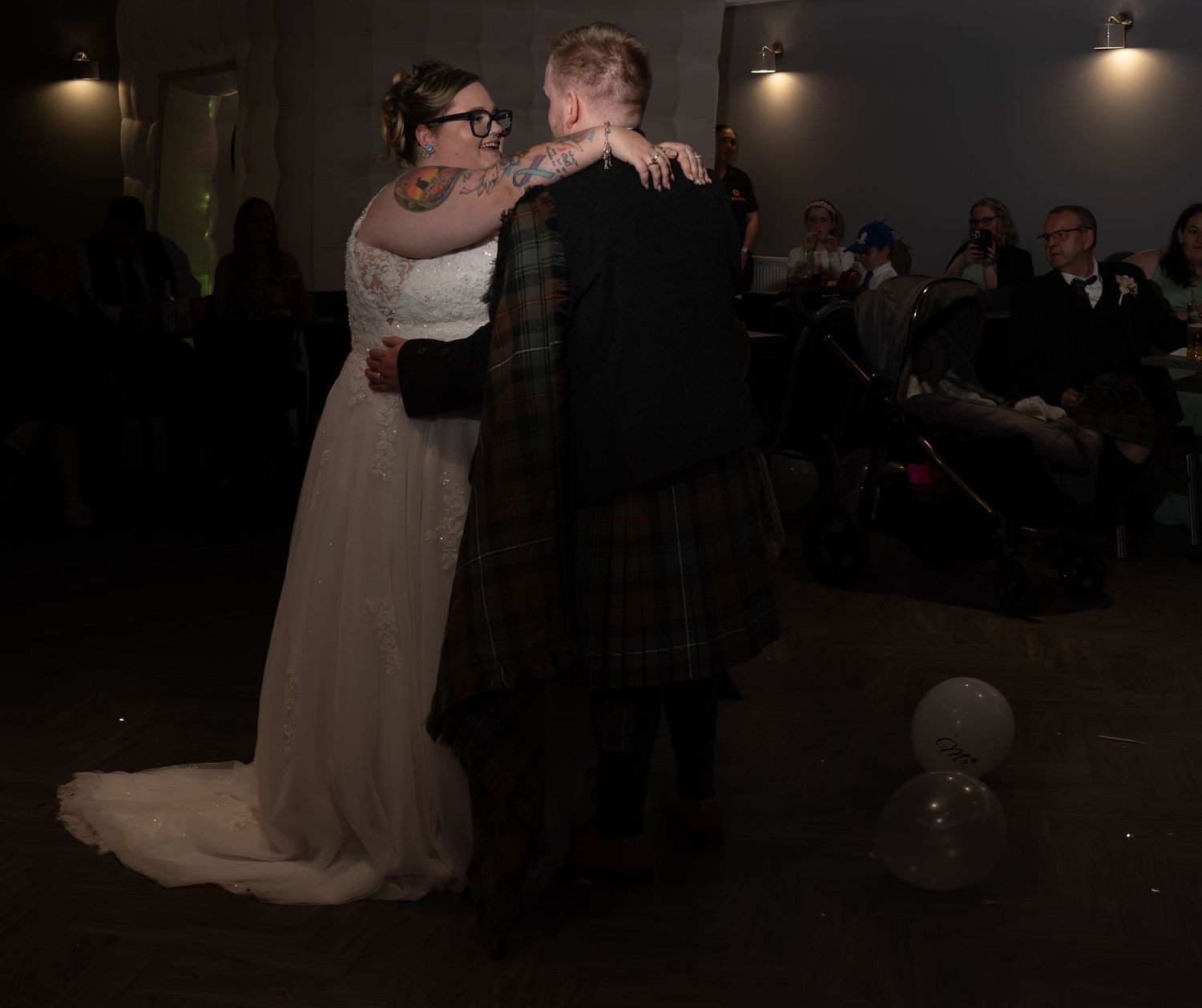 Couple shares their first dance at a wedding reception with the groom wearing a traditional Scottish kilt.