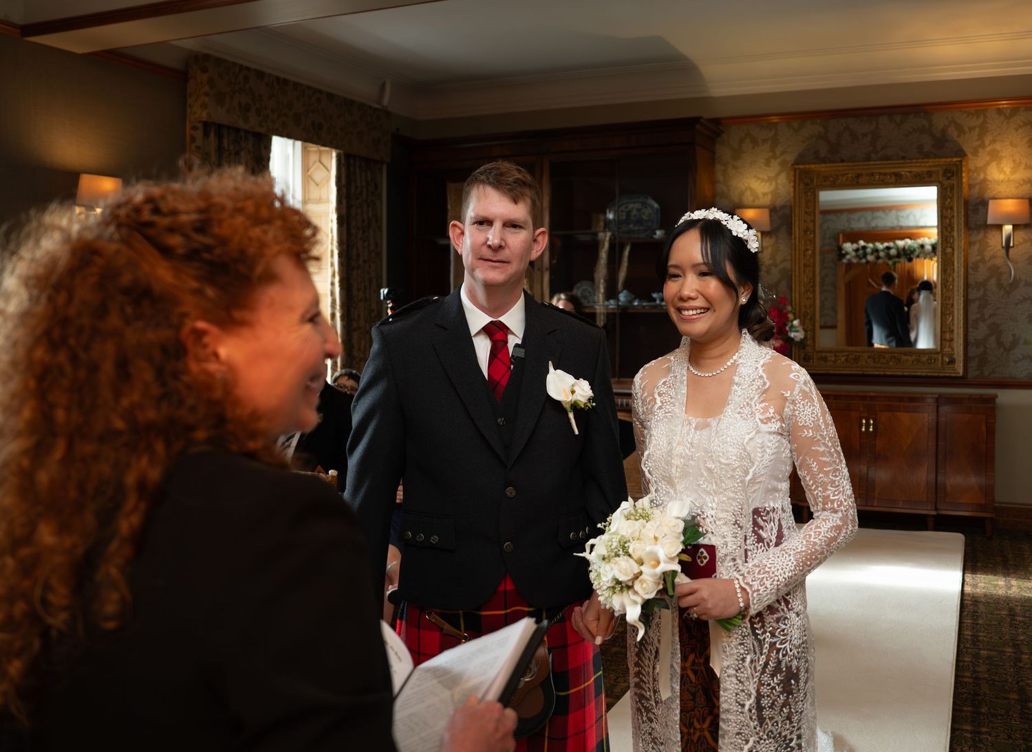 Wedding guests dance and celebrate together in a warm-lit reception hall with elegant decor and rustic stone walls.