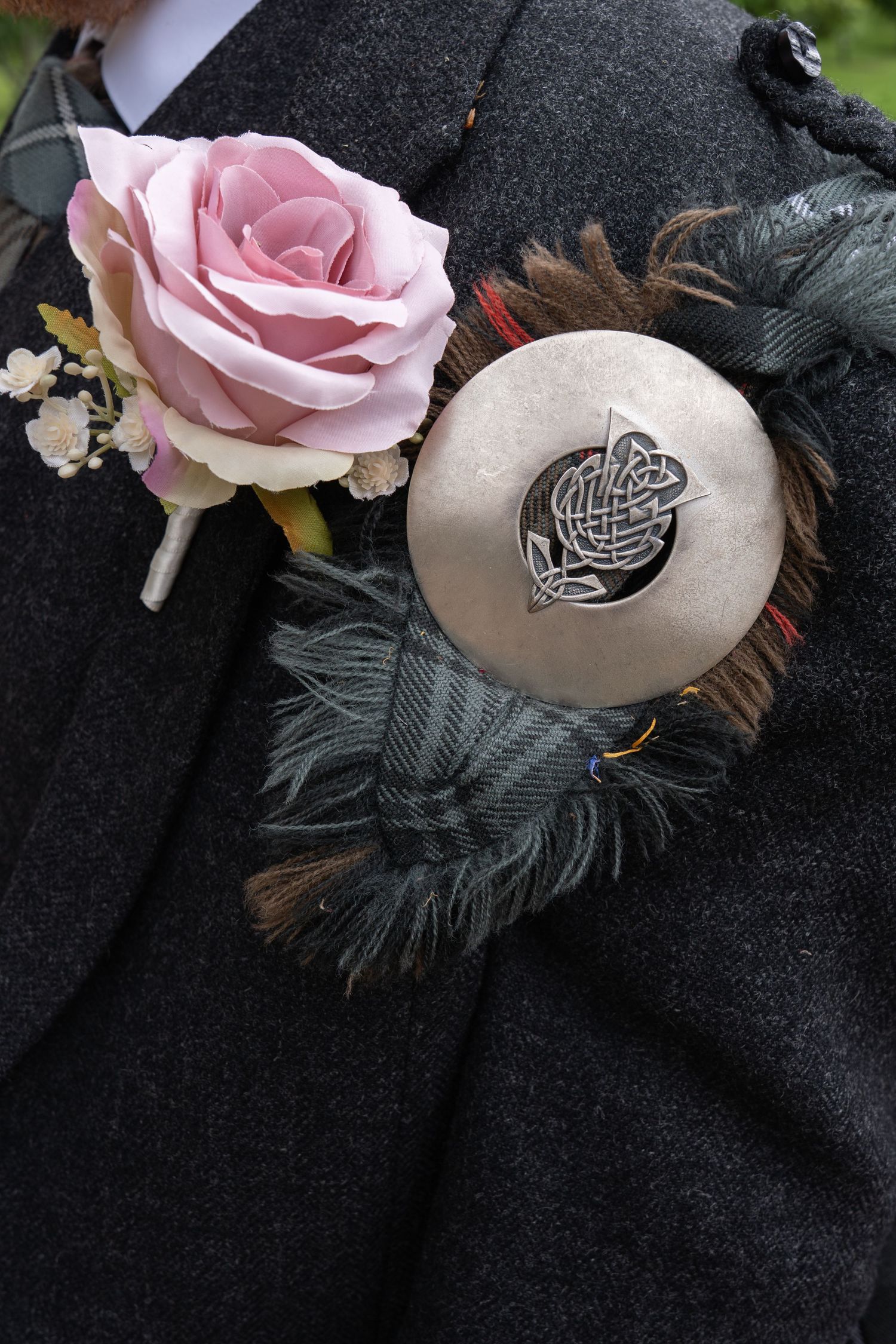 A pink rose boutonniere with Celtic brooch pin against dark formal wear.