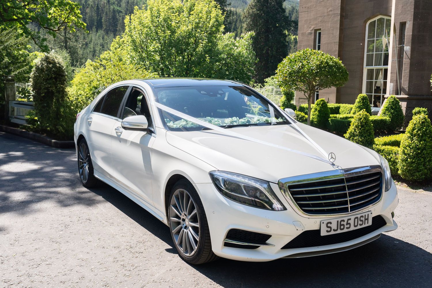 White Mercedes S-Class decorated with wedding ribbons parked in elegant driveway.