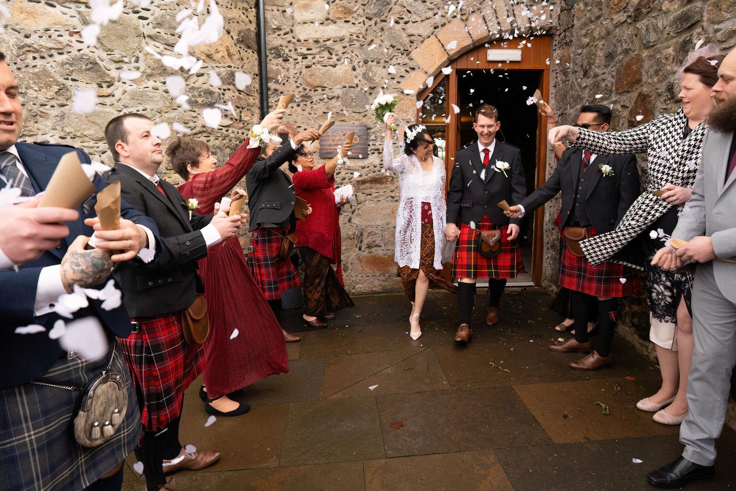 Wedding guests dancing and mingling in rustic stone venue with warm lighting and festive atmosphere.