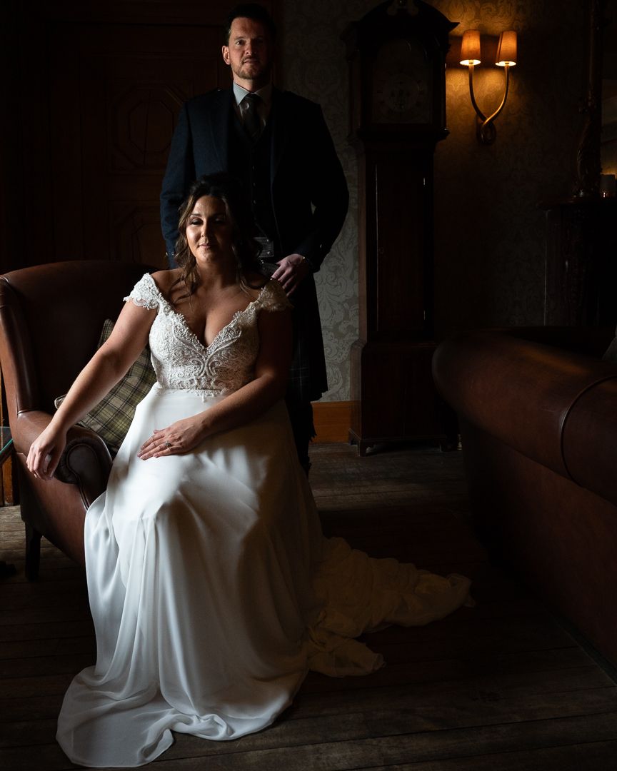 Dramatic moody bridal portraits captured in dark room with window light highlighting white wedding dress.