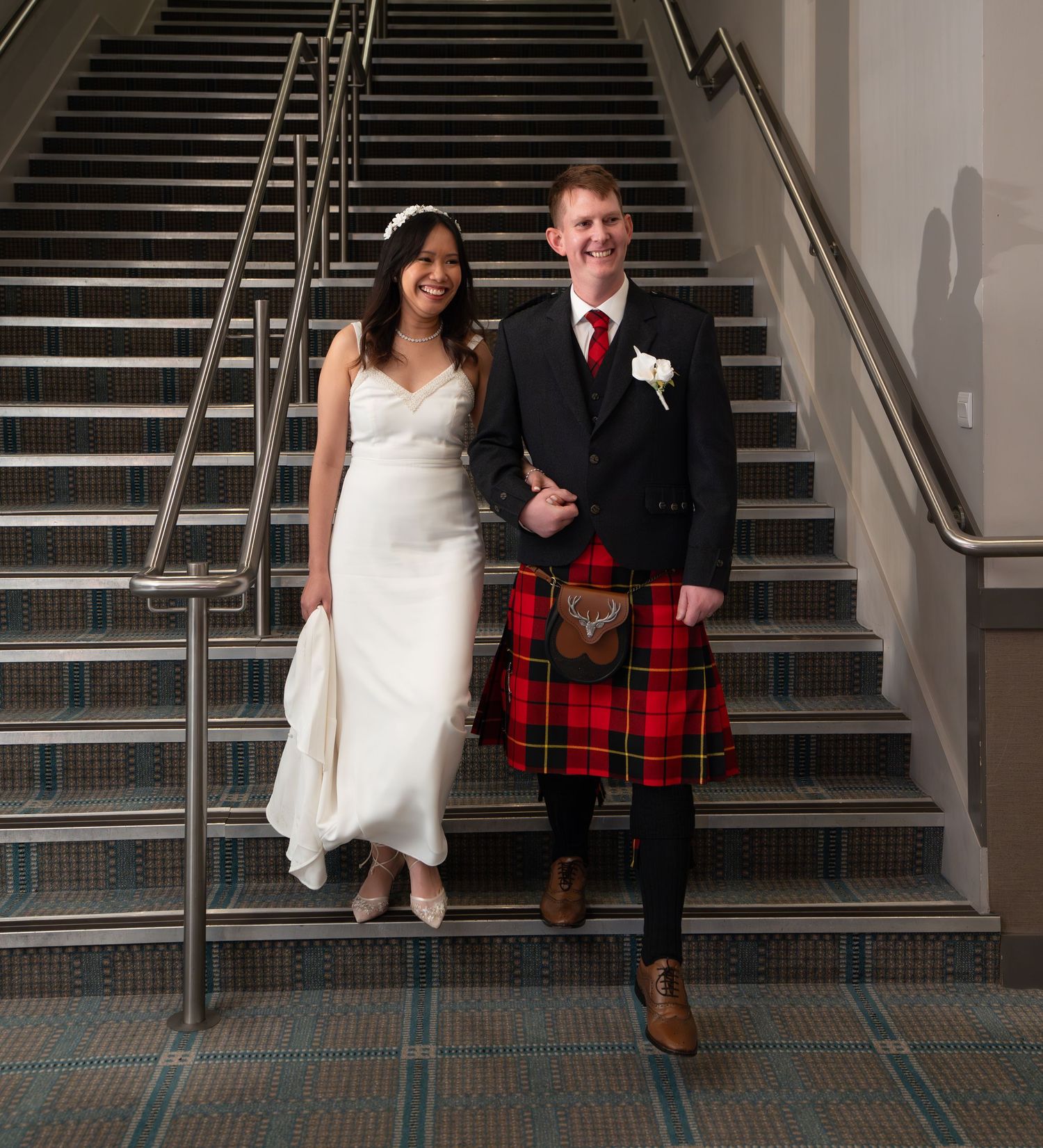 Couple sitting on stairs in wedding attire with groom wearing traditional red plaid tartan kilt.