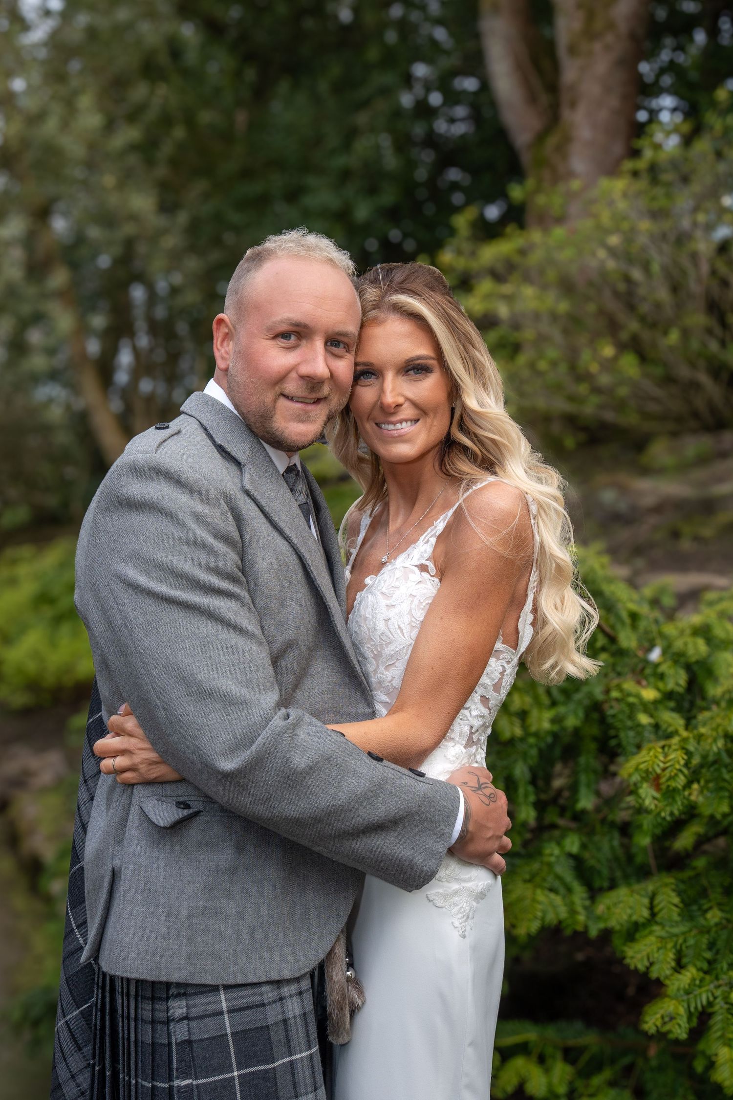 Wedding couple embracing outdoors, groom wearing traditional Scottish kilt and gray jacket.