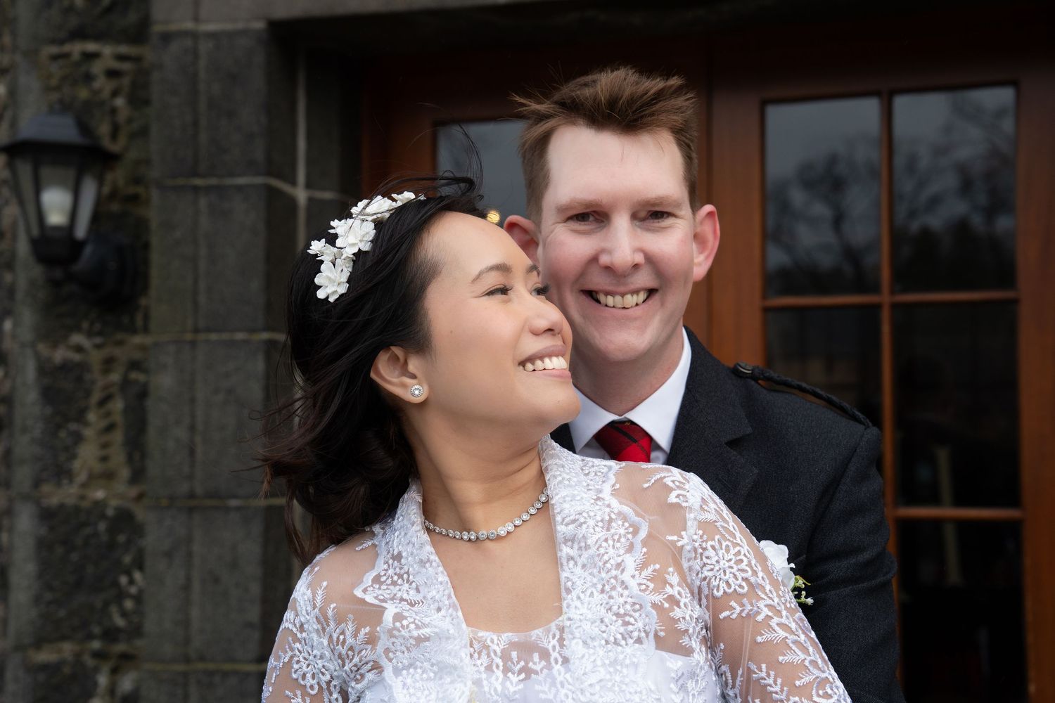 Happy couple share candid laughing moment together on their wedding day outside historic stone building.