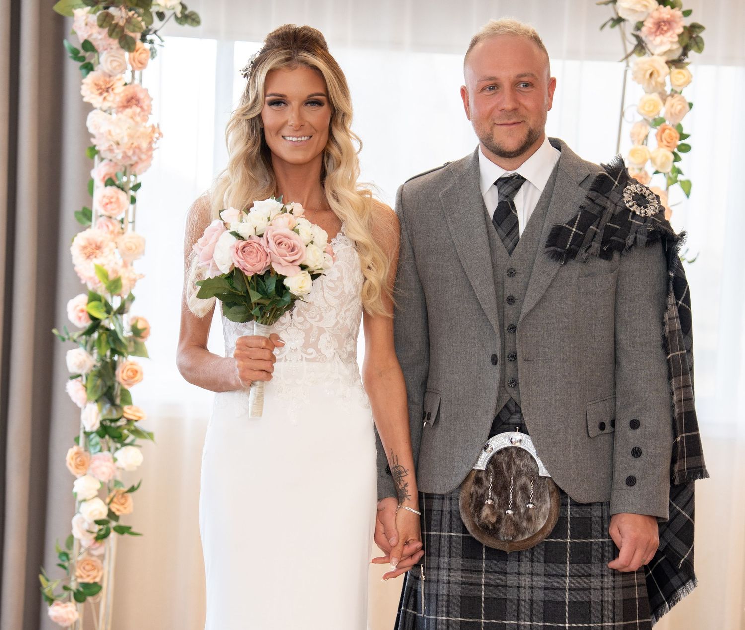 Wedding party poses under floral arch with elegant decor and vintage styling.