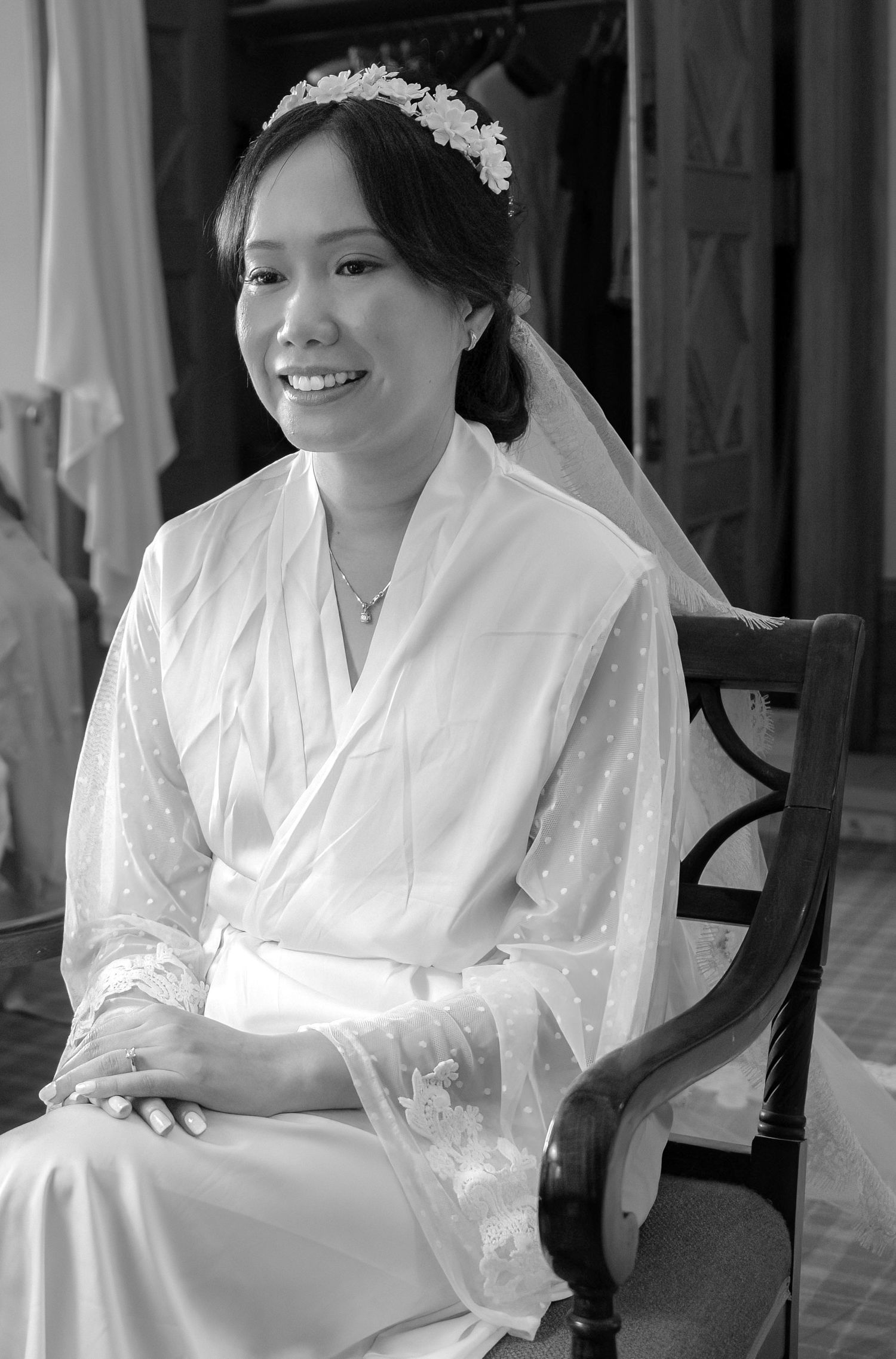 A bride in a white silk robe sits gracefully while getting ready for her wedding day.