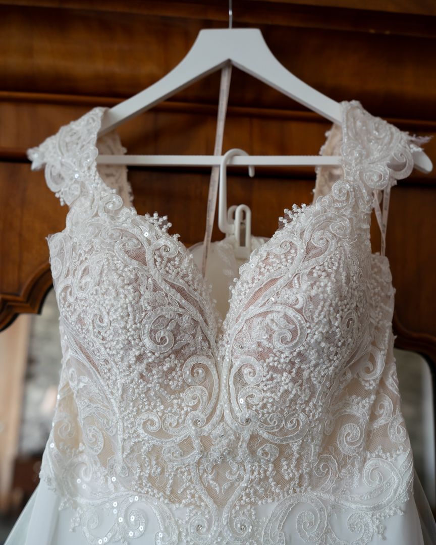 Close-up details of delicate white lace and beading on a wedding dress bodice hanging on white hangers.
