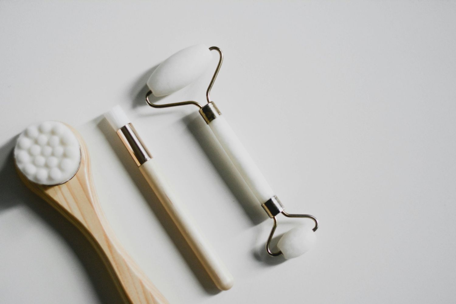 Minimalist wooden facial massage tools and jade roller against white surface showing natural skincare tools.