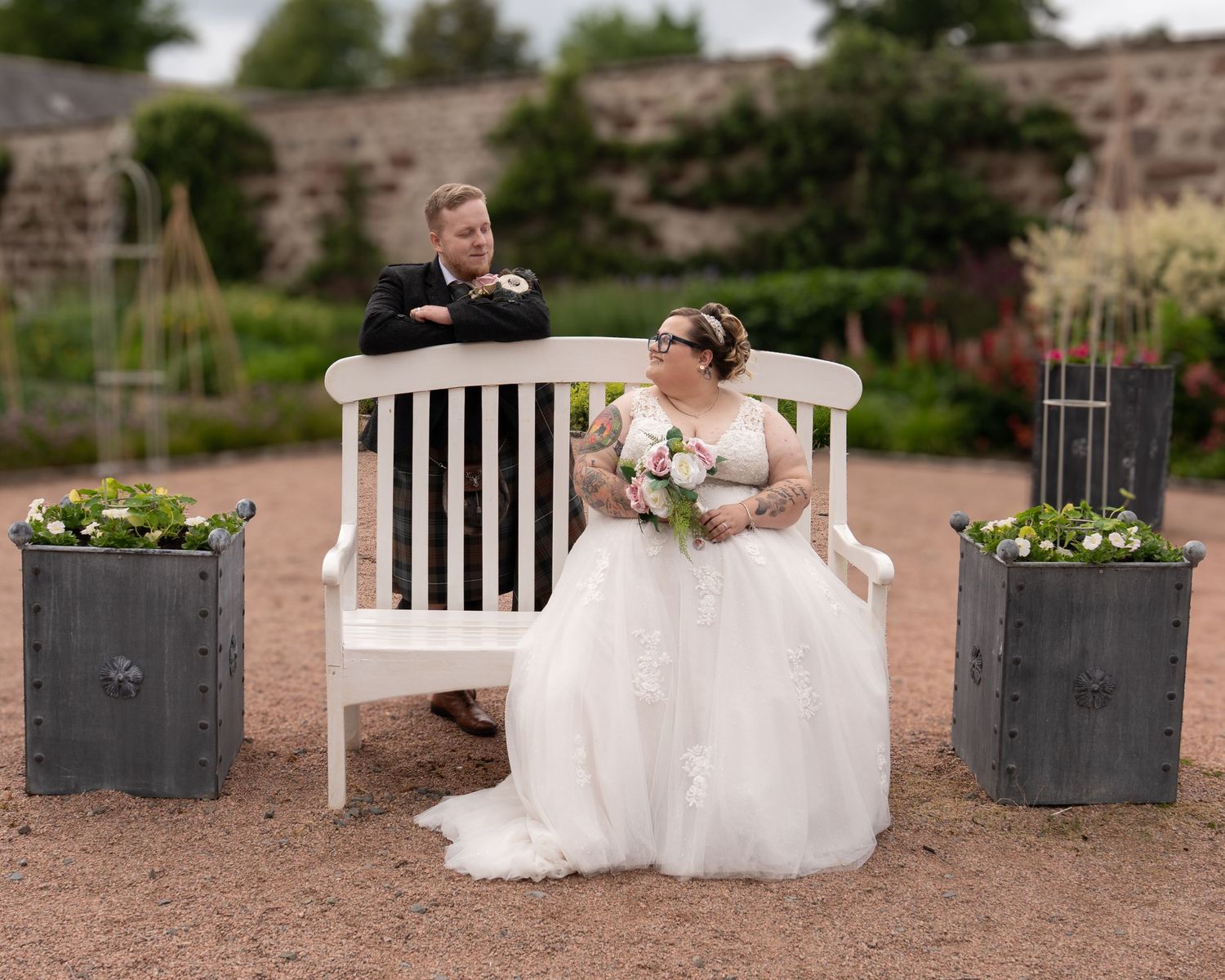 A scenic wedding portrait session in a garden patio area with white benches and decorative planters.