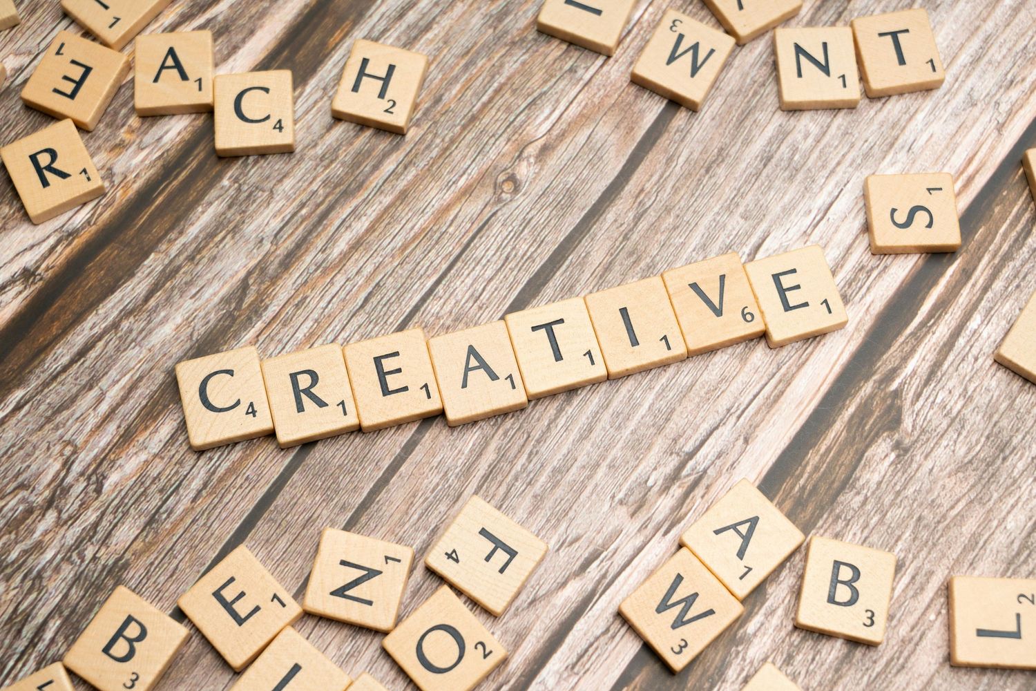 Wooden Scrabble letter tiles spelling out the word CREATIVE on rustic wooden surface.