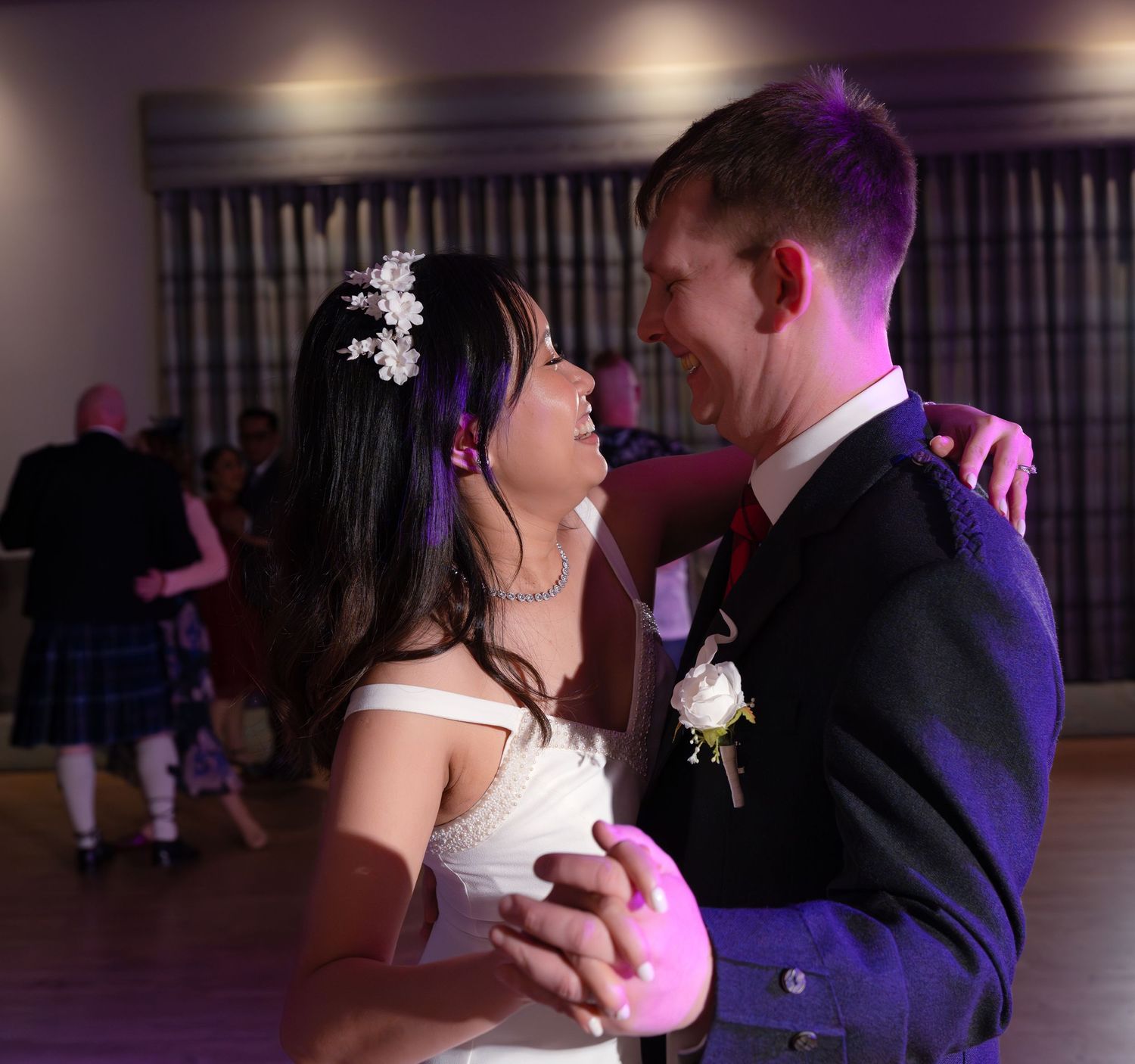A newlywed couple dancing together at their wedding reception, with purple lighting in the background.