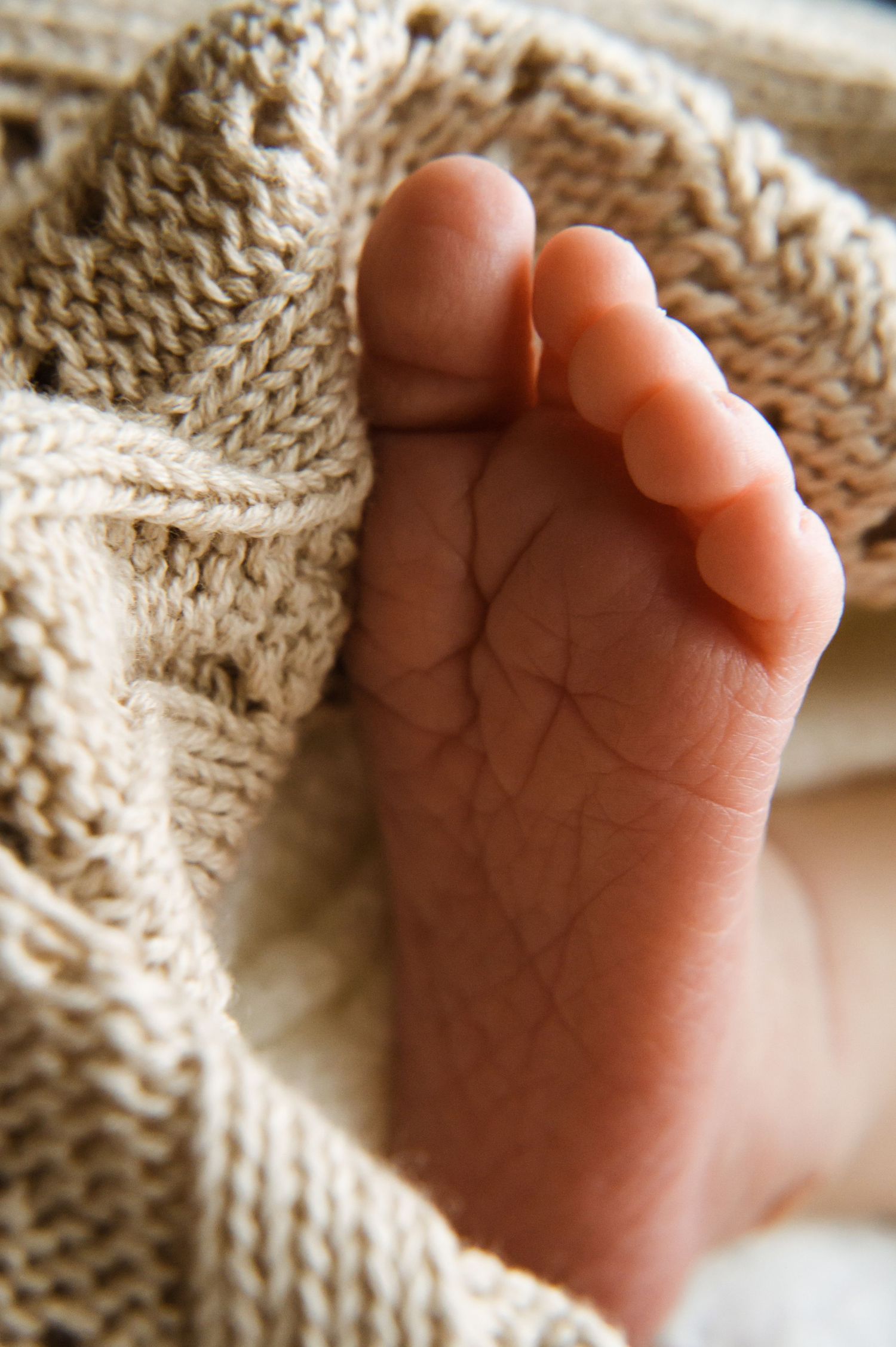 Tiny baby foot nestled in soft knitted beige blanket showing delicate skin texture and tiny toes.