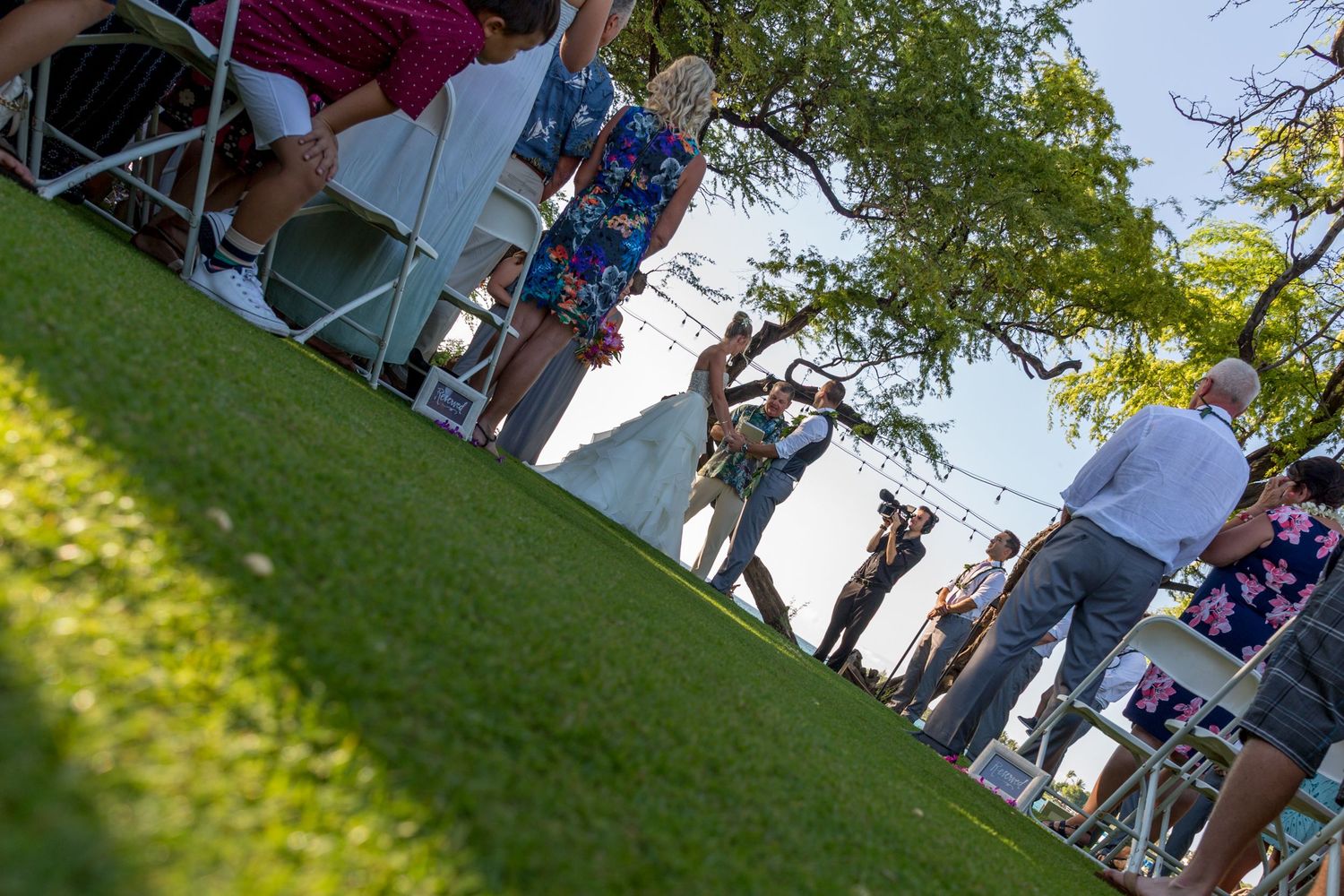People walking and interacting at an outdoor community event with vendor booths and green lawn in the sunshine.