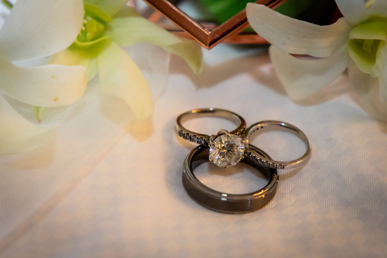 Wedding rings displayed on white flower petals with elegant lighting.