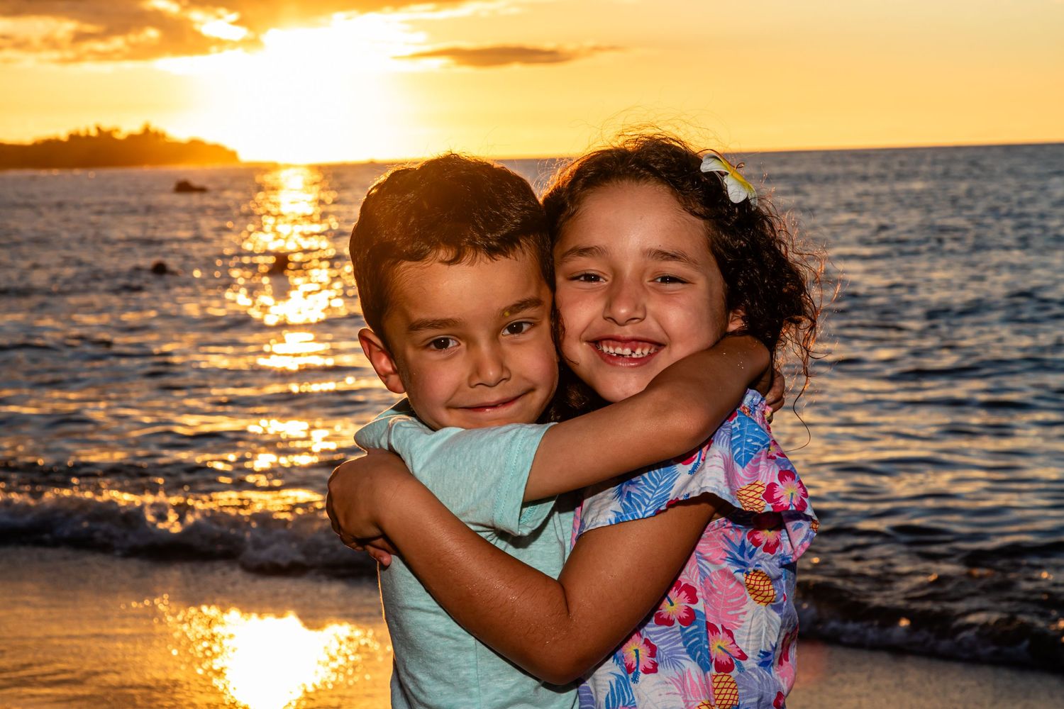 Children hugging and laughing during golden hour sunset on a beach near Kailua Kona.