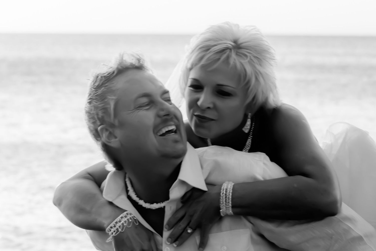 Two people share a tender embrace while lounging at a sunny beach in black and white photography.