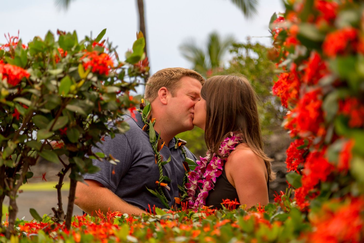 A couple shares a kiss among tropical flowers with Hawaiian leis in Kona, Hawaii.