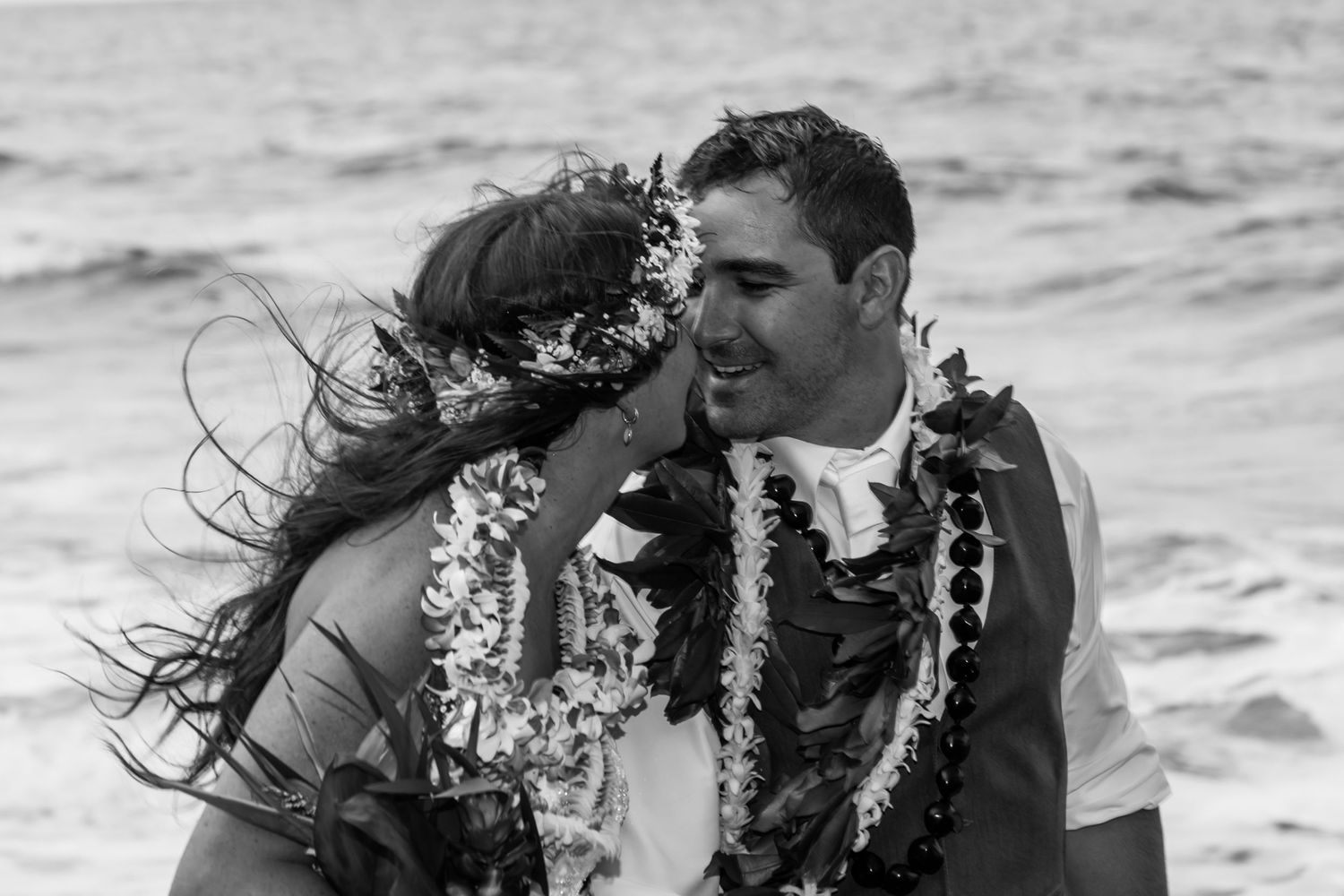 A black and white beach wedding photo with traditional Hawaiian leis and ocean waves at Waipio Valley on the Big Island of Hawaii.