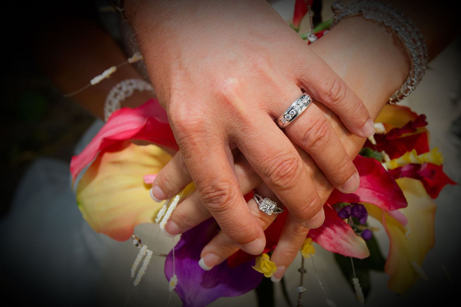 A diamond engagement ring sparkles on a hand holding colorful tropical flowers.
