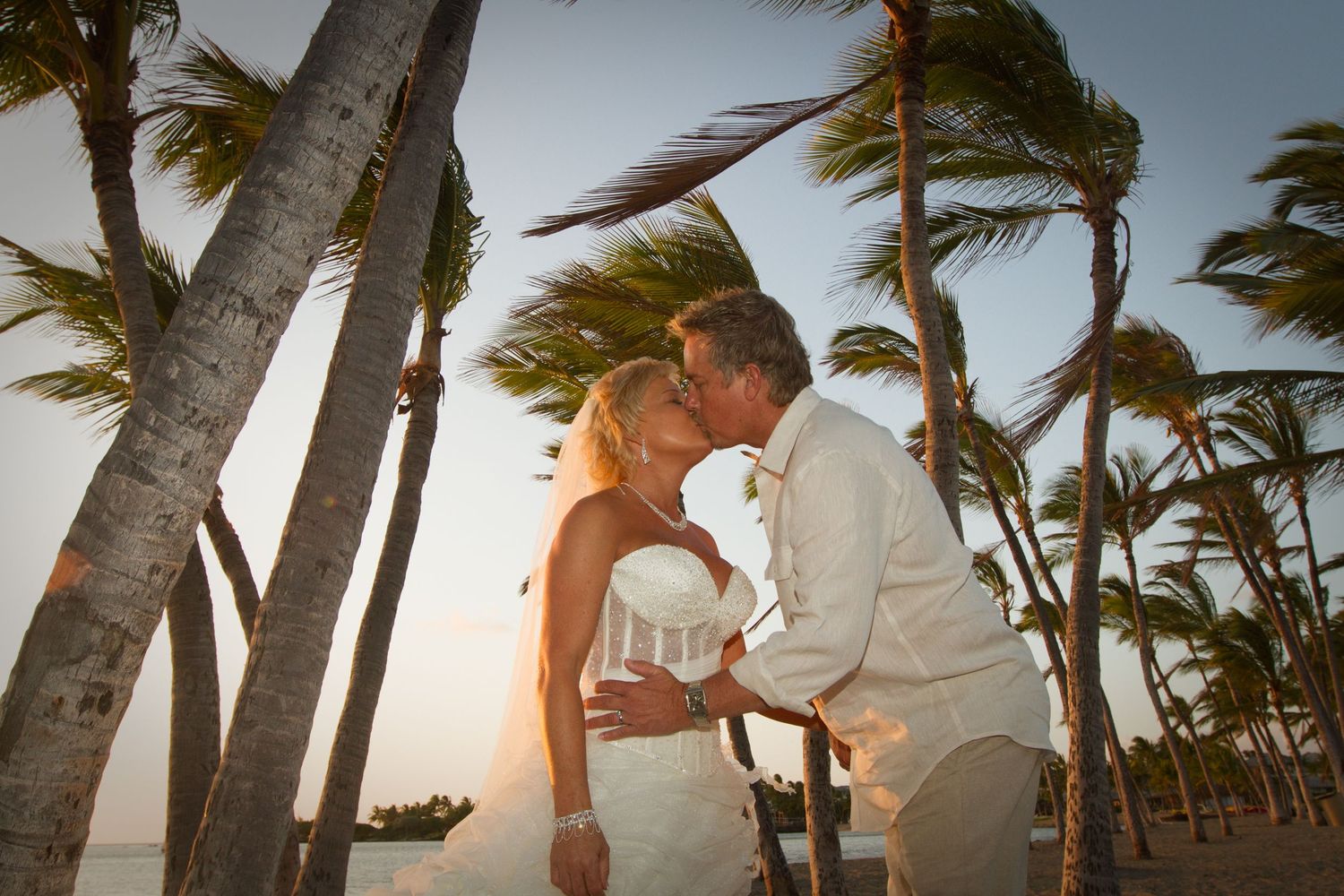 A romantic moment under swaying palm trees on a tropical beach at sunset.
