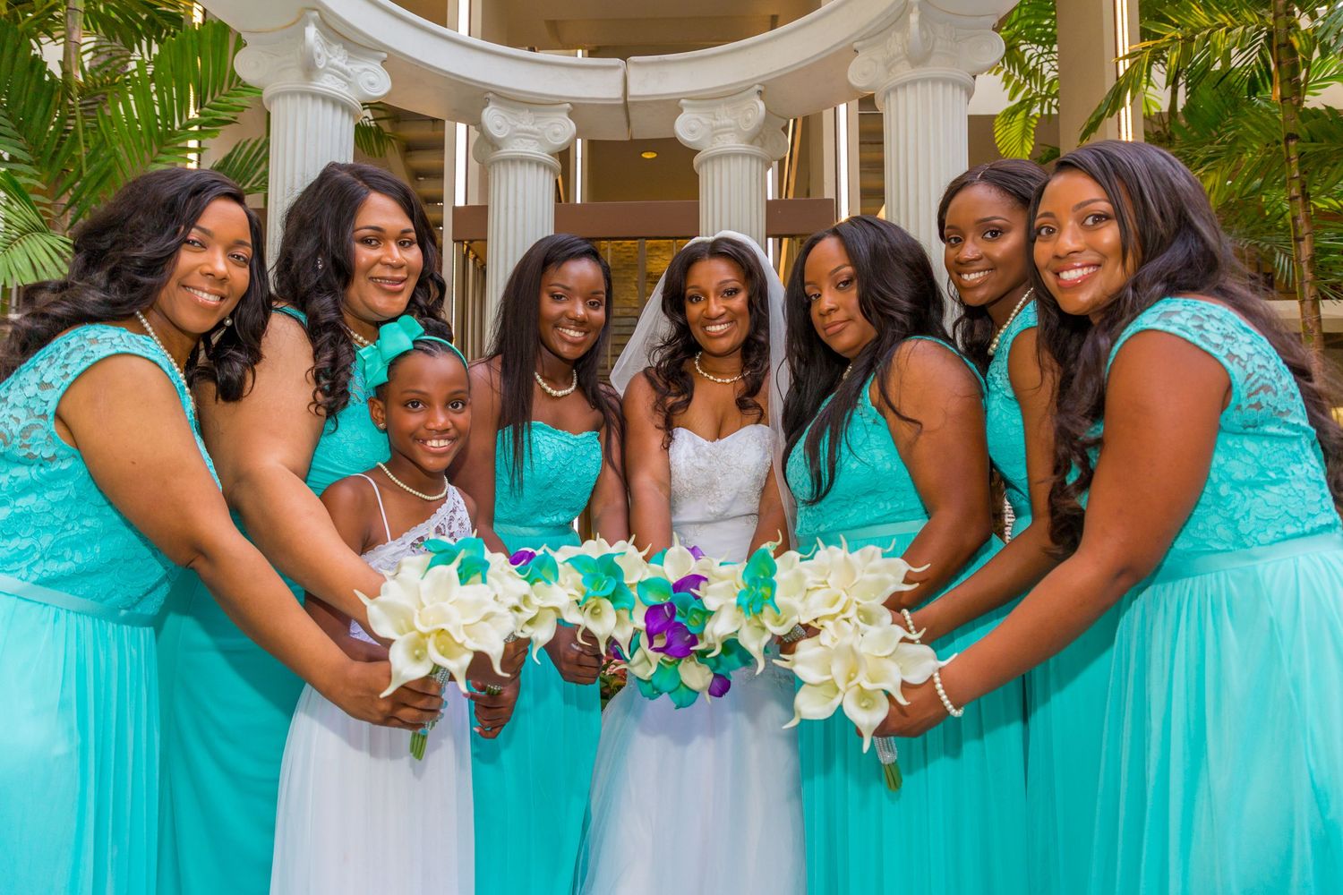 Bridesmaids in turquoise dresses gather around bride holding white bouquets at the Hilton Waikiki Beach hotel in Honolulu, Hawaii.