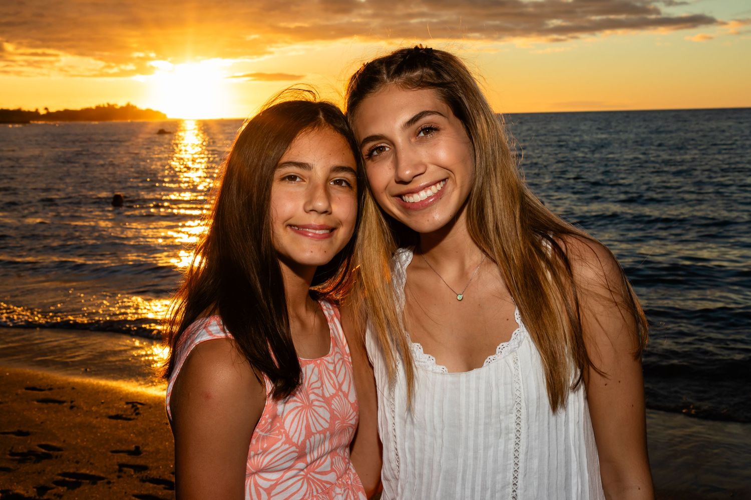 Two people embracing on a beach at sunset with golden light reflecting on the ocean near Kailua Kona.