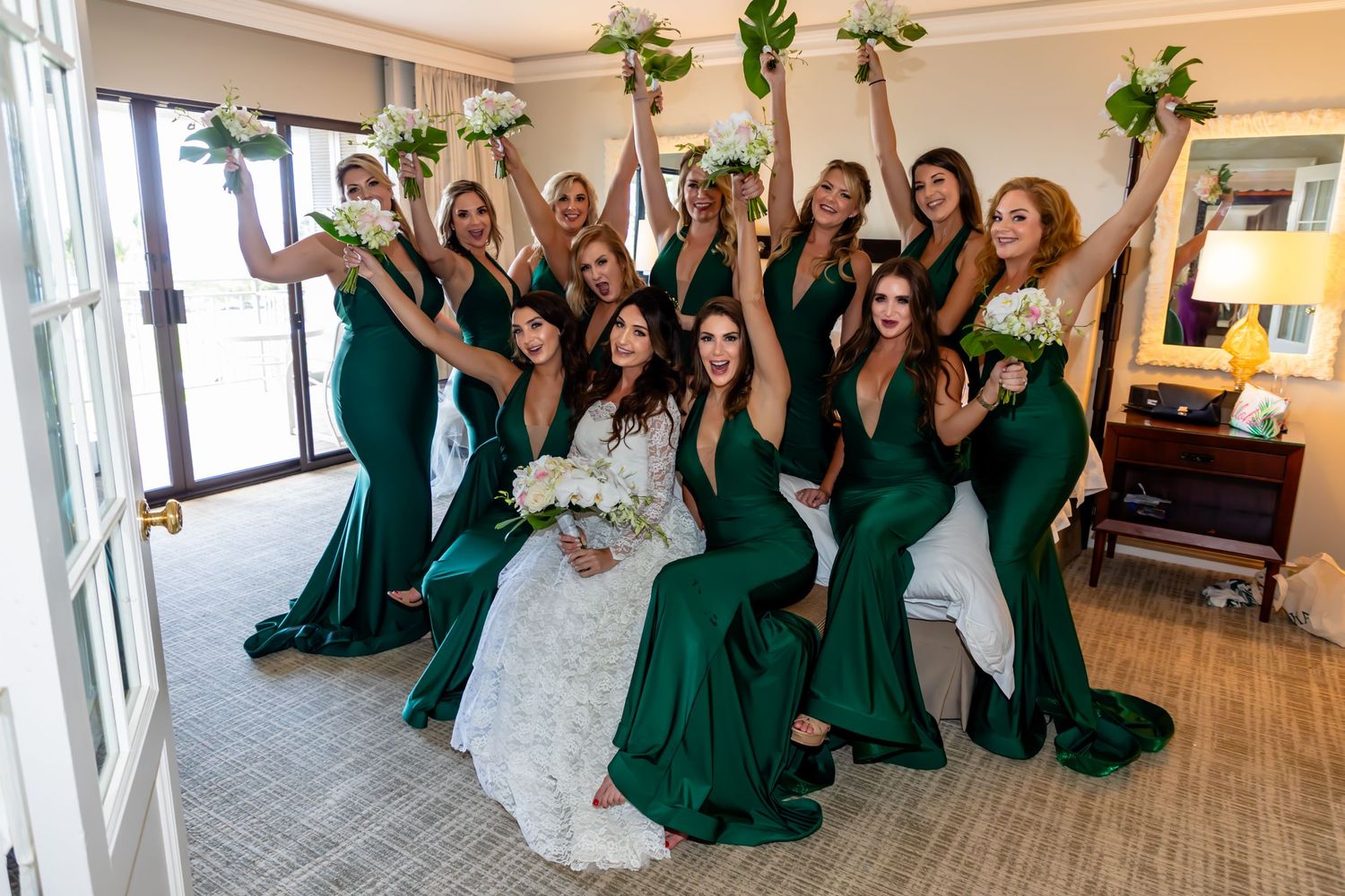 Wedding party in emerald green dresses poses joyfully in a bright room at the Fairmont Orchid at Mauna Lani near Kailua Kona.