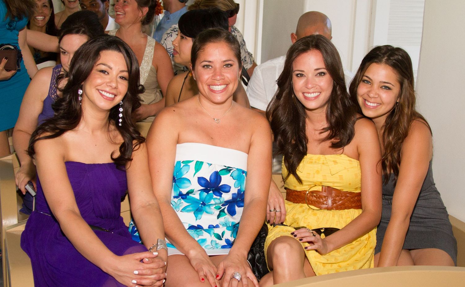 A group in formal attire sits together at a wedding in Kona, wearing purple, floral print, and yellow dresses.