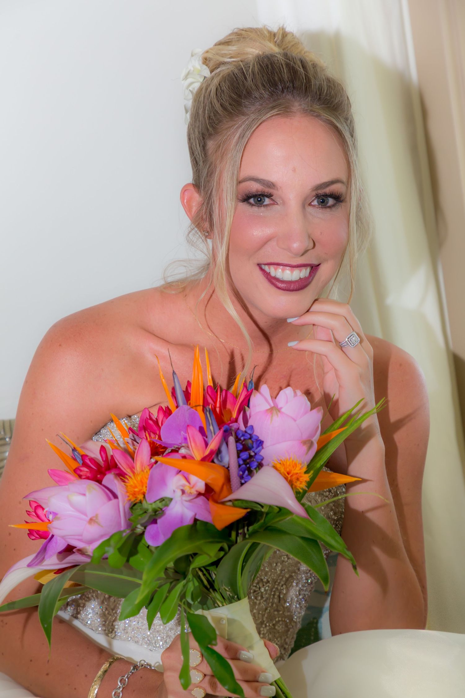 Elegant bride in strapless gown poses with vibrant tropical bouquet featuring pink and orange flowers and greenery.