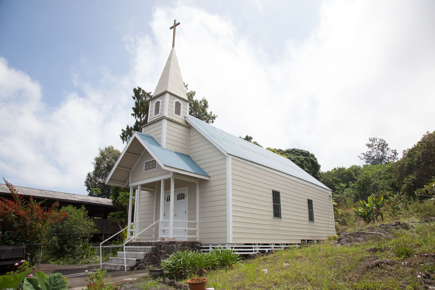 Historic white chapel with steeple on hillside surrounded by lush Hawaiian landscape.