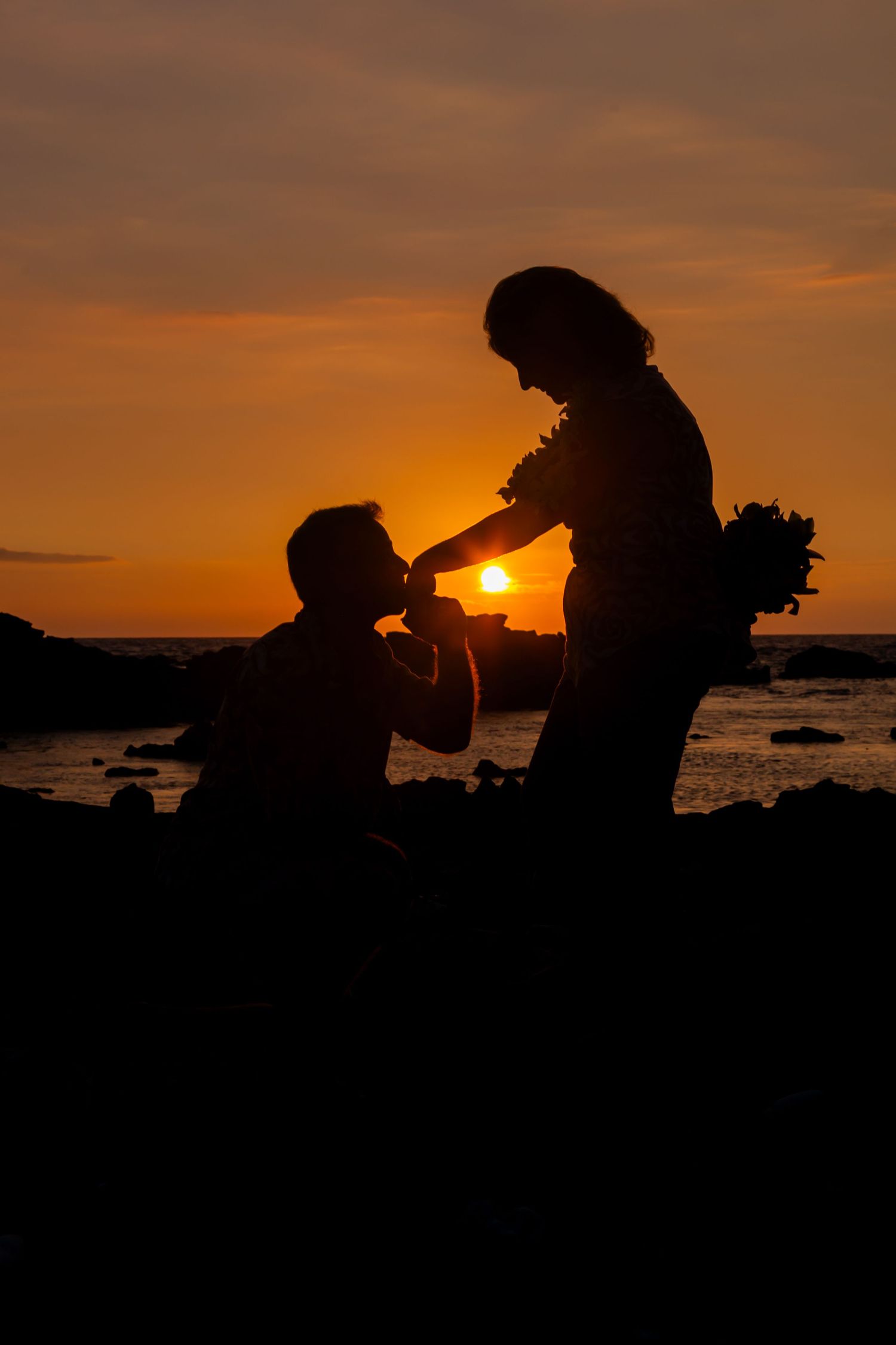 A silhouetted couple sharing a romantic moment at sunset by the ocean at Anaehoomalu Bay beach near Kailua Kona.