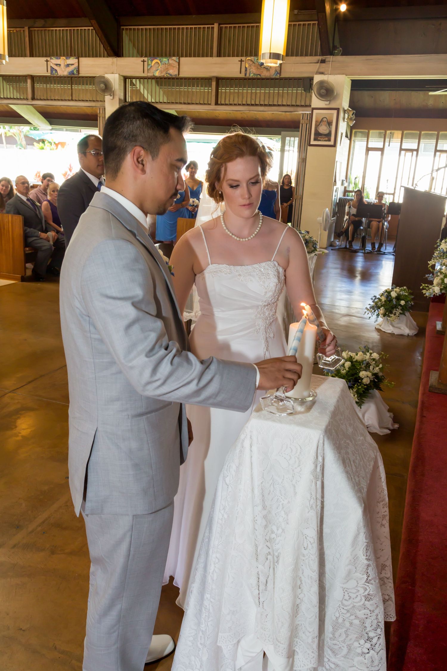 A wedding couple lighting a unity candle during their Honolulu Catholic church, Our Lady of Sorrows, in Oahu, Hawaii.