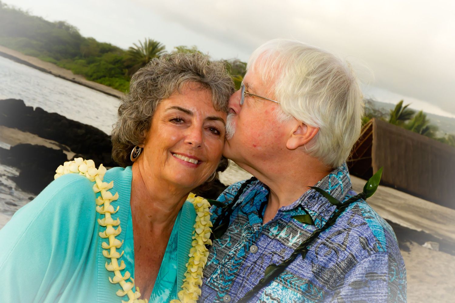 Loving couple in tropical attire share tender moment against ocean backdrop at Konokohau beach in Kailua Kona.