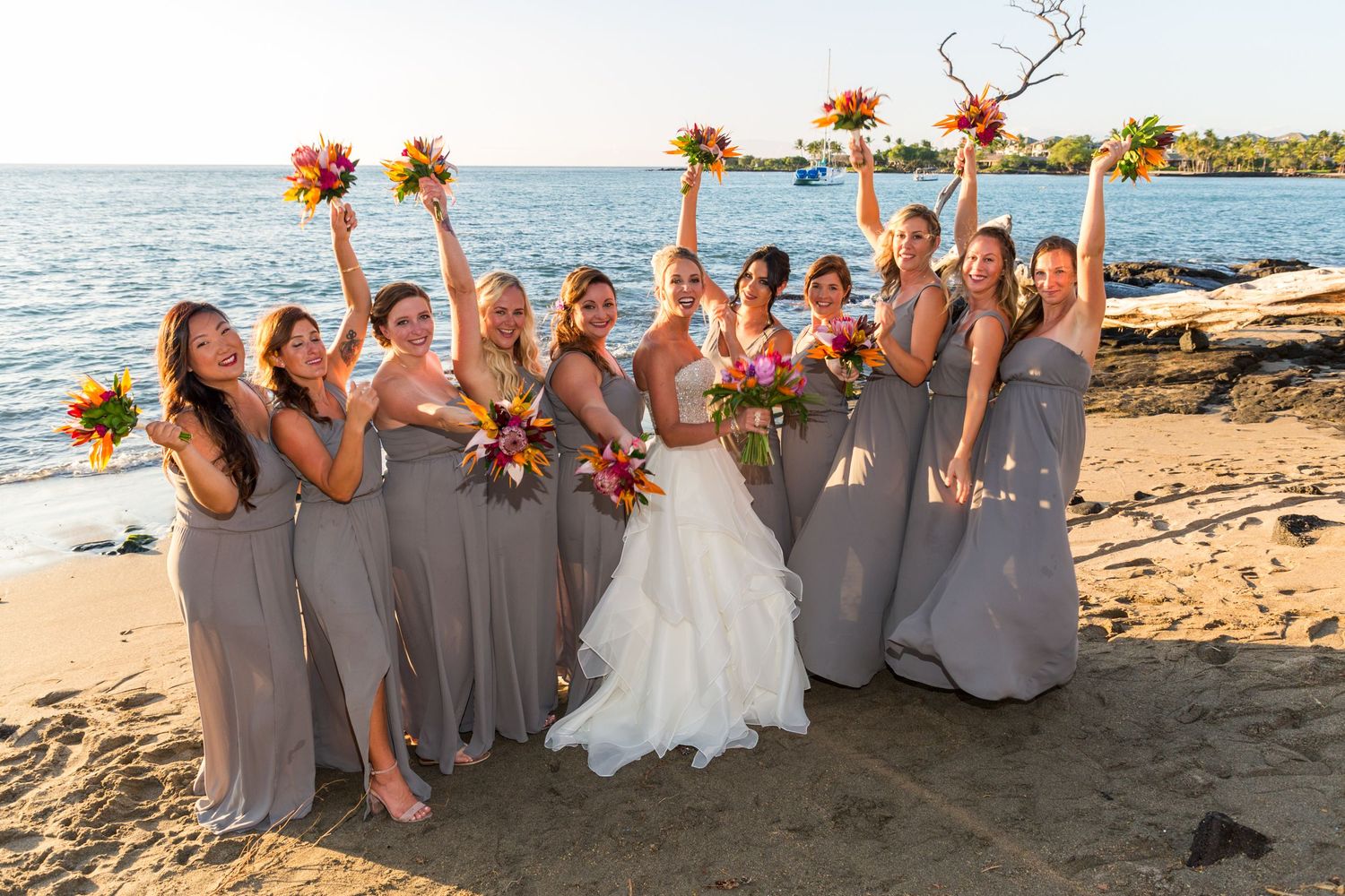 Bridesmaids in gray dresses celebrating with the bride on a tropical beach in Hawaii.