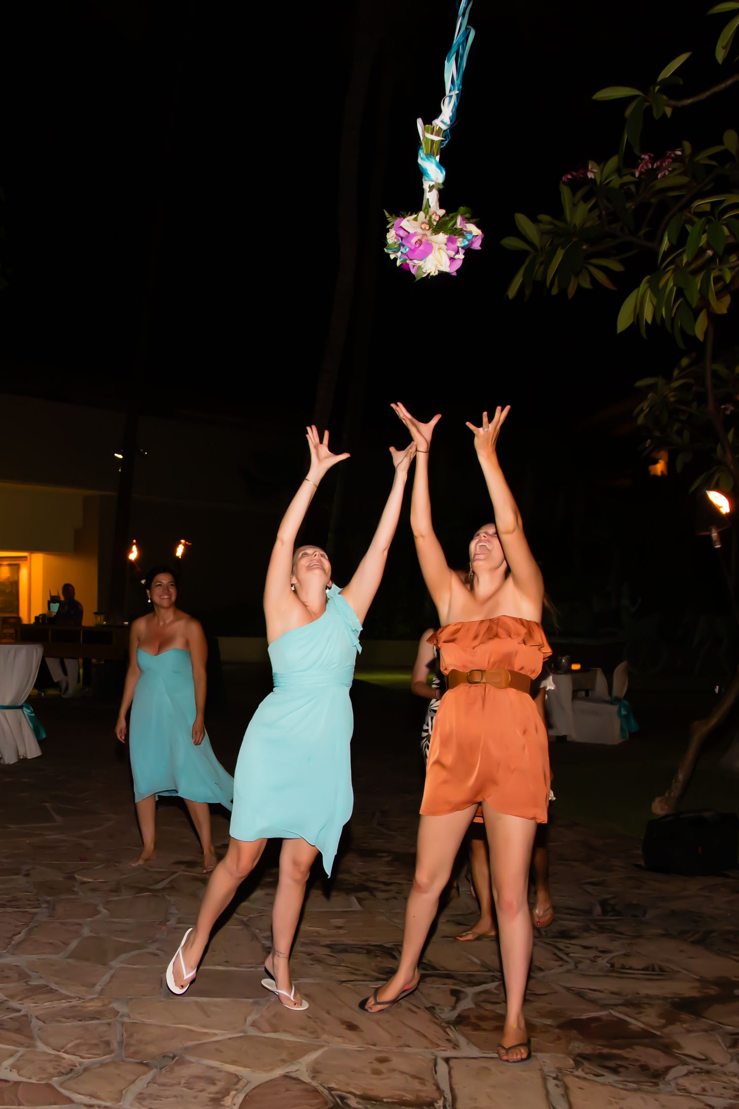 Wedding guests jumping to catch a bouquet toss at an outdoor evening reception at a wedding in Kona, Hawaii.